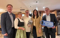 Fünf Personen stehen nebeneinander. Ein Mann hält ein Logoschild in seinen Händen, eine Person hält ein Kochbuch in seinen Händen.