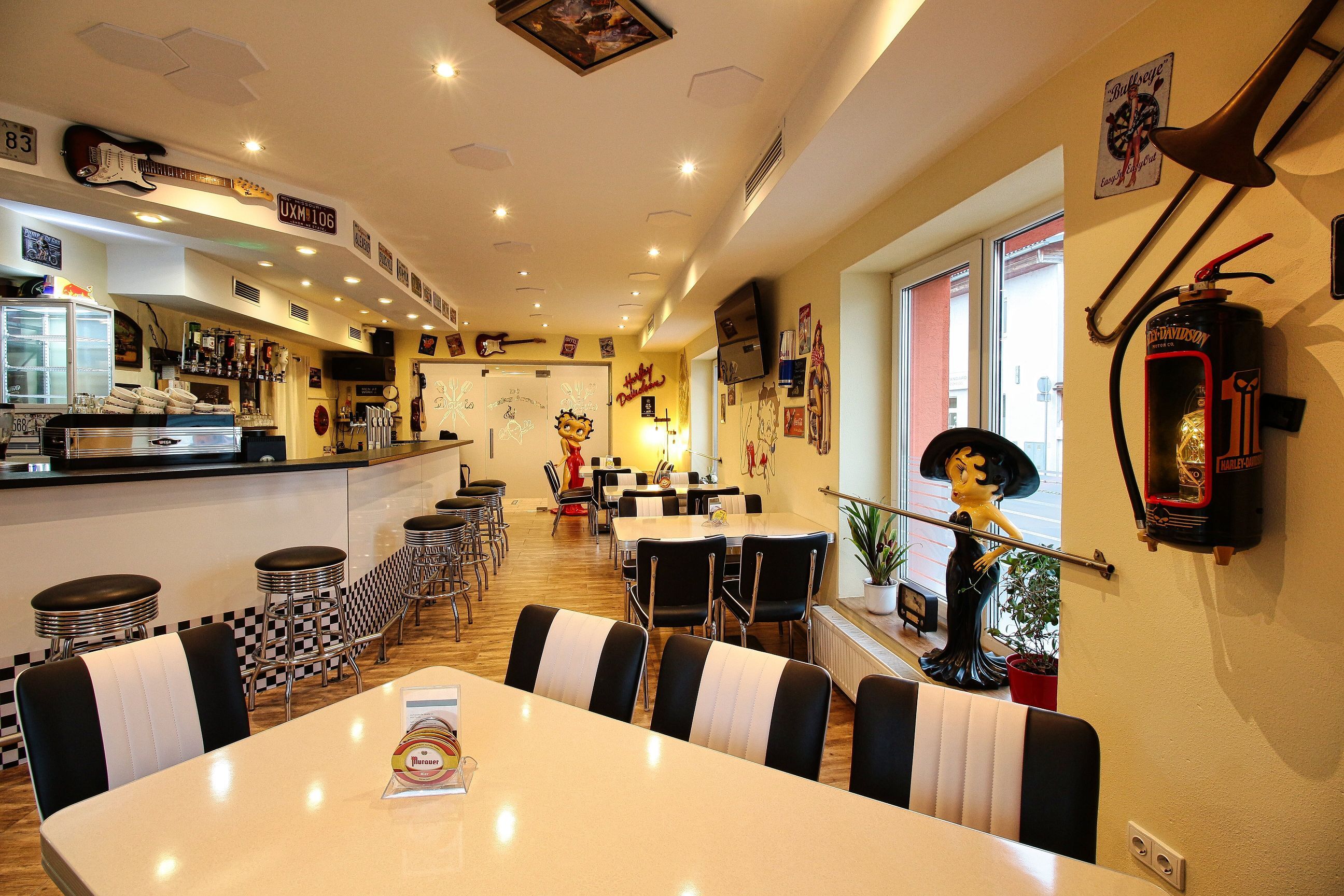 Innenansicht eines Rockabilly-Cafés mit Retro-Dekor, Barhockern und Tischen.