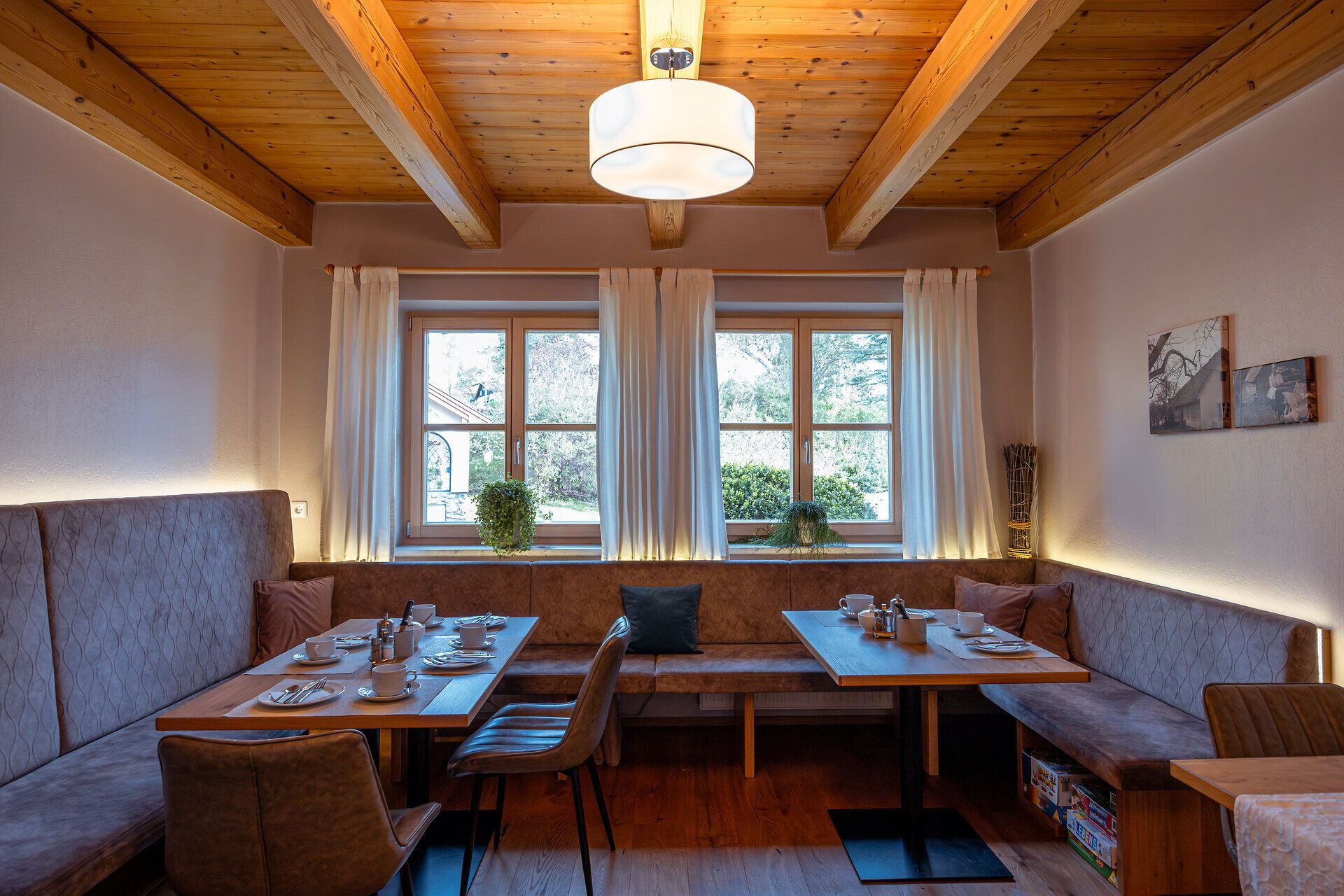 In einem einladenden Raum mit warmem Holz und sanftem Licht genießen Gäste eine gemütliche Atmosphäre. Die Tische sind liebevoll gedeckt und laden dazu ein, regionale Köstlichkeiten zu probieren, während die Natur draußen in voller Pracht erblüht.
