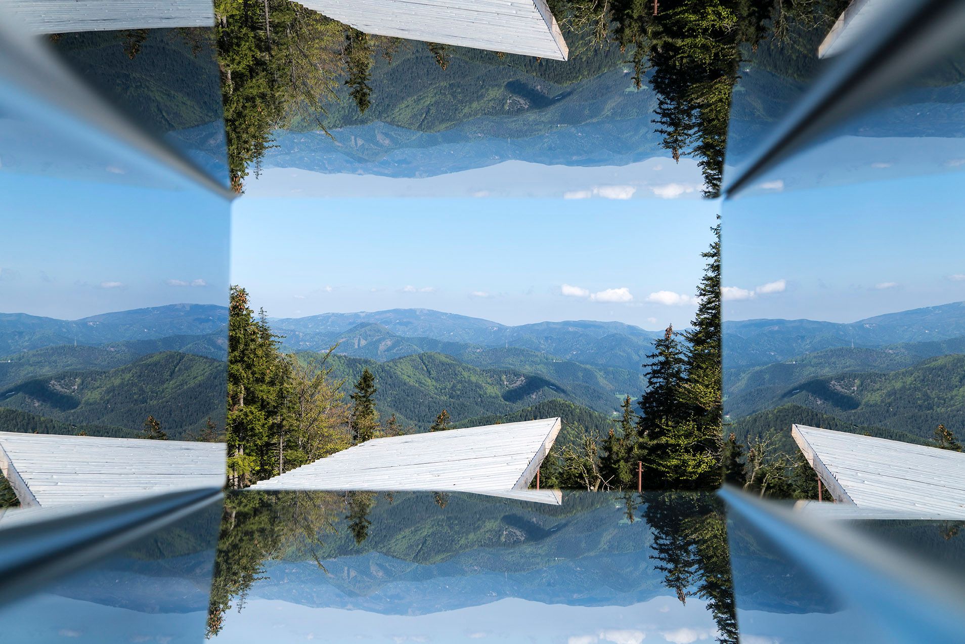 Spiegelbild eines Bergpanoramas mit Bäumen und blauen Himmel.