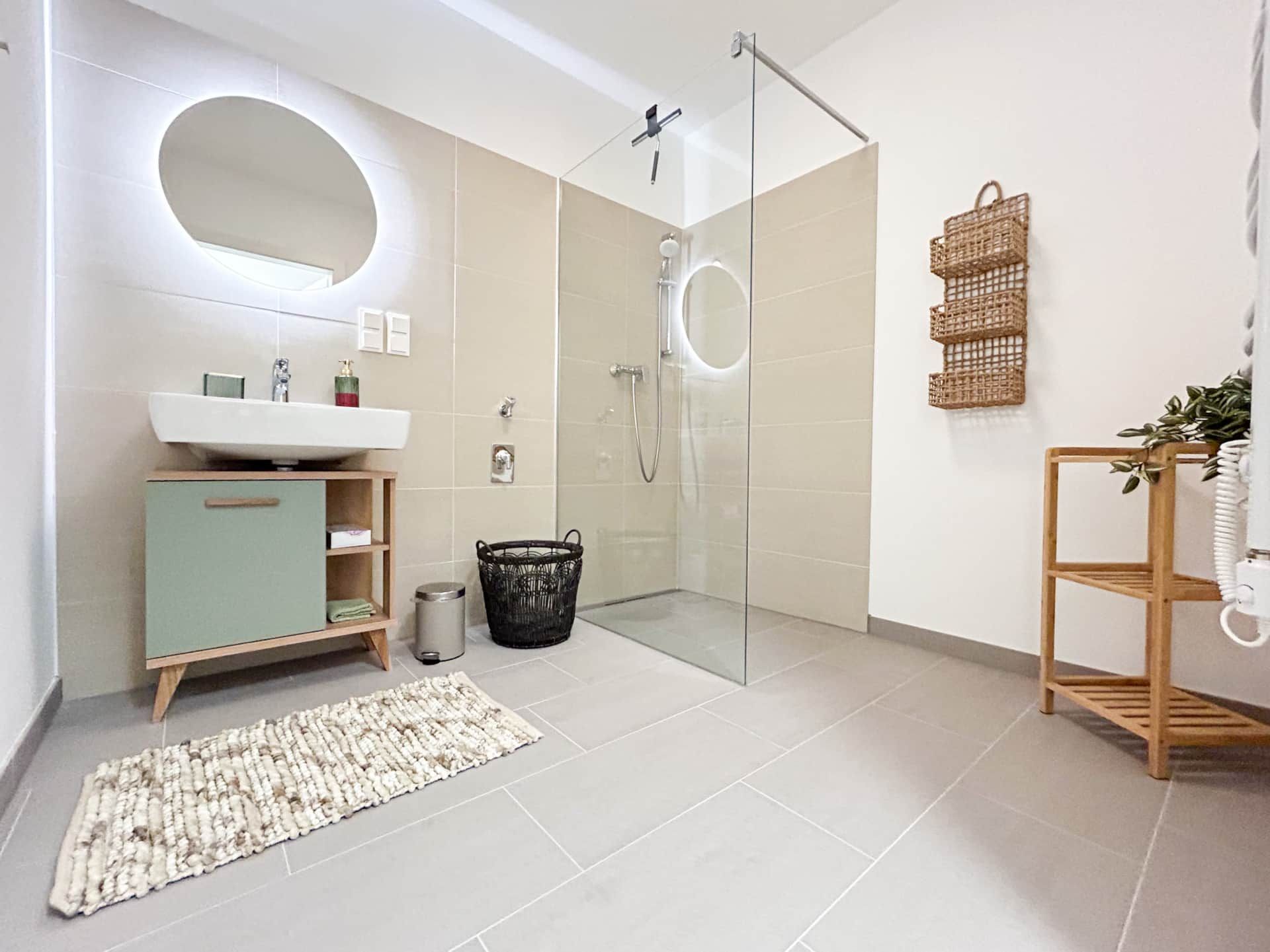 Bright, large bathroom with walk-in shower, washbasin, vanity unit, towels and illuminated mirror