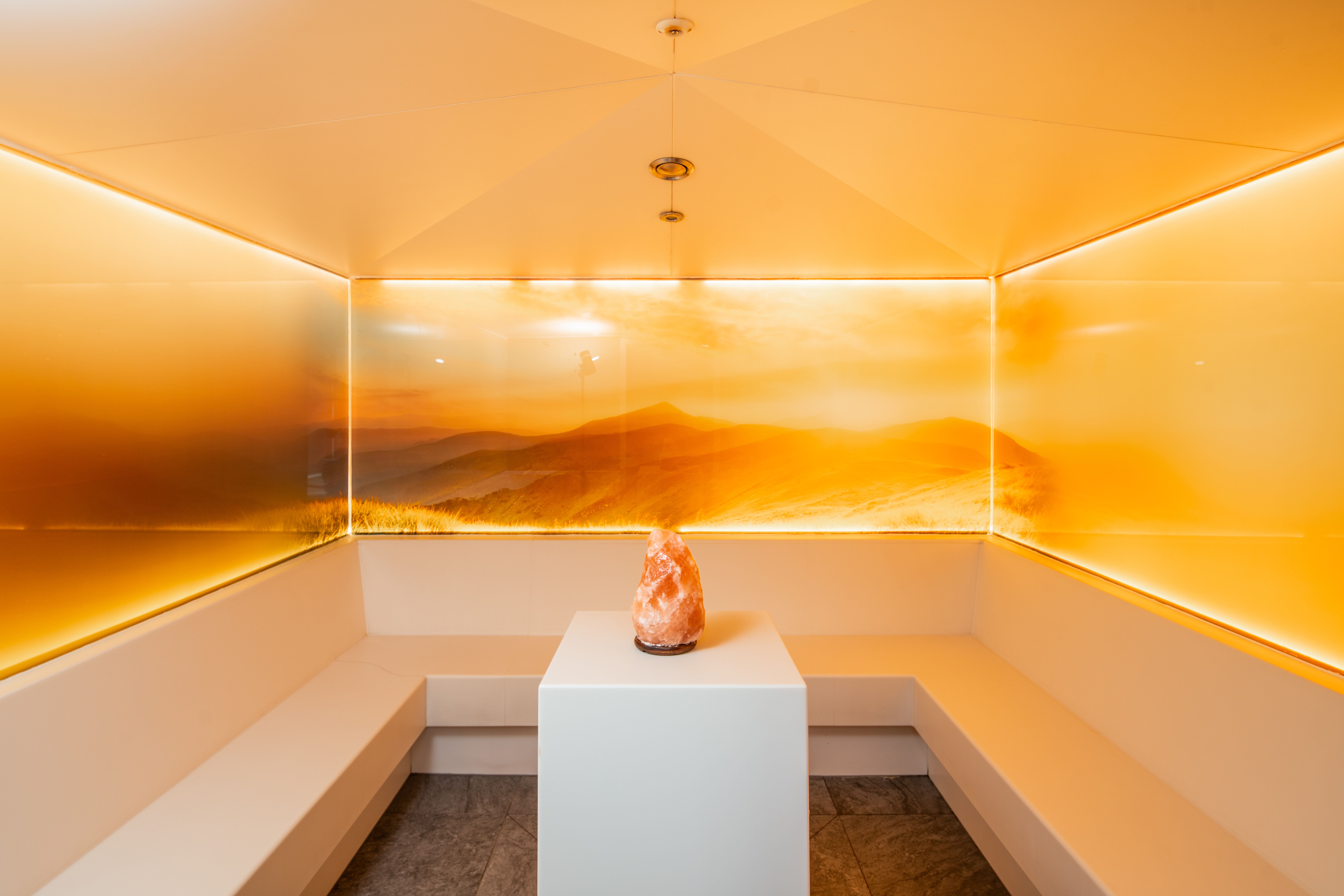 Ein moderner Wellnessraum mit orange beleuchteten Wänden und einem Salzstein auf einem Tisch in der Mitte.