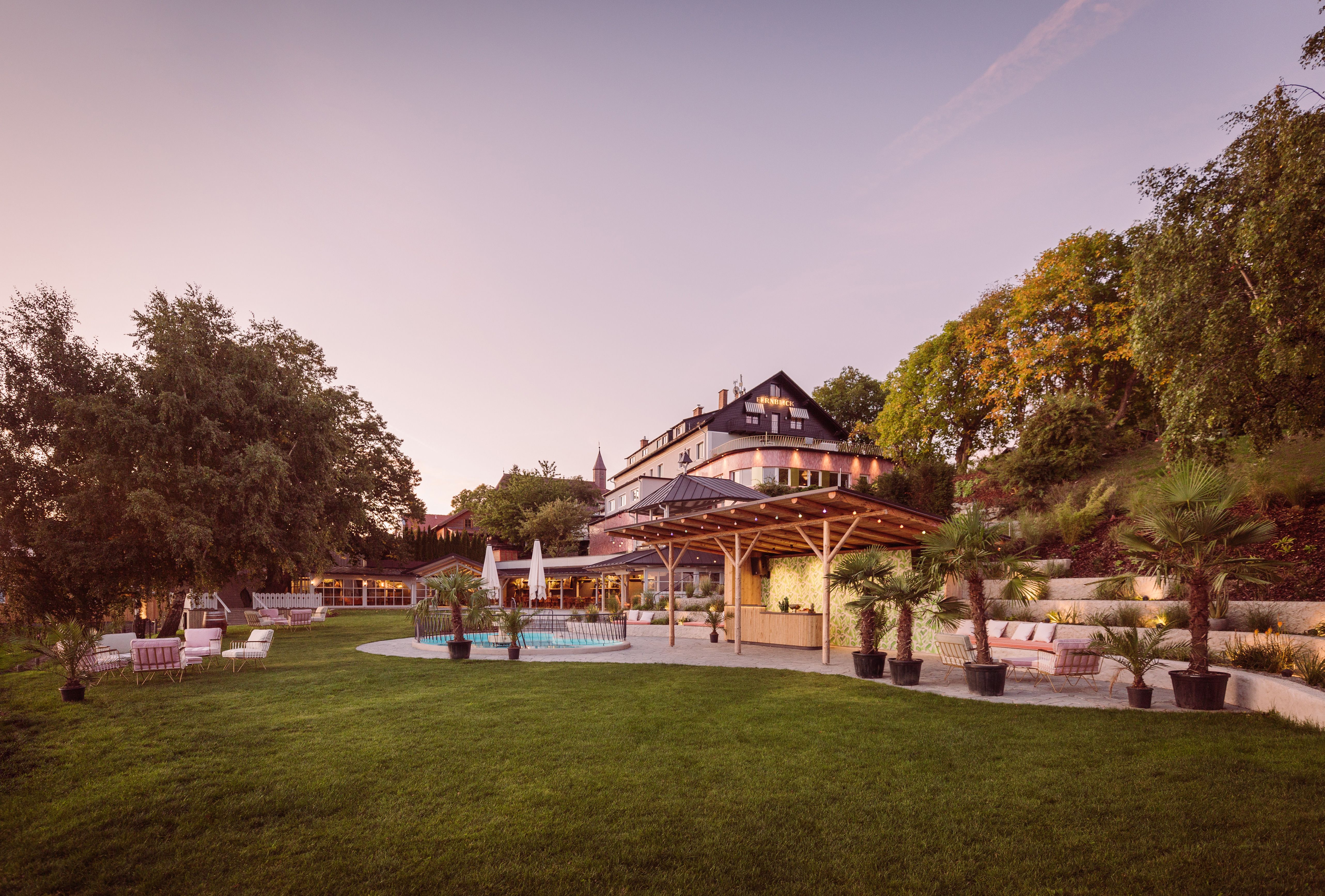Ein großes Gebäude mit Terrasse und Garten bei Sonnenuntergang.