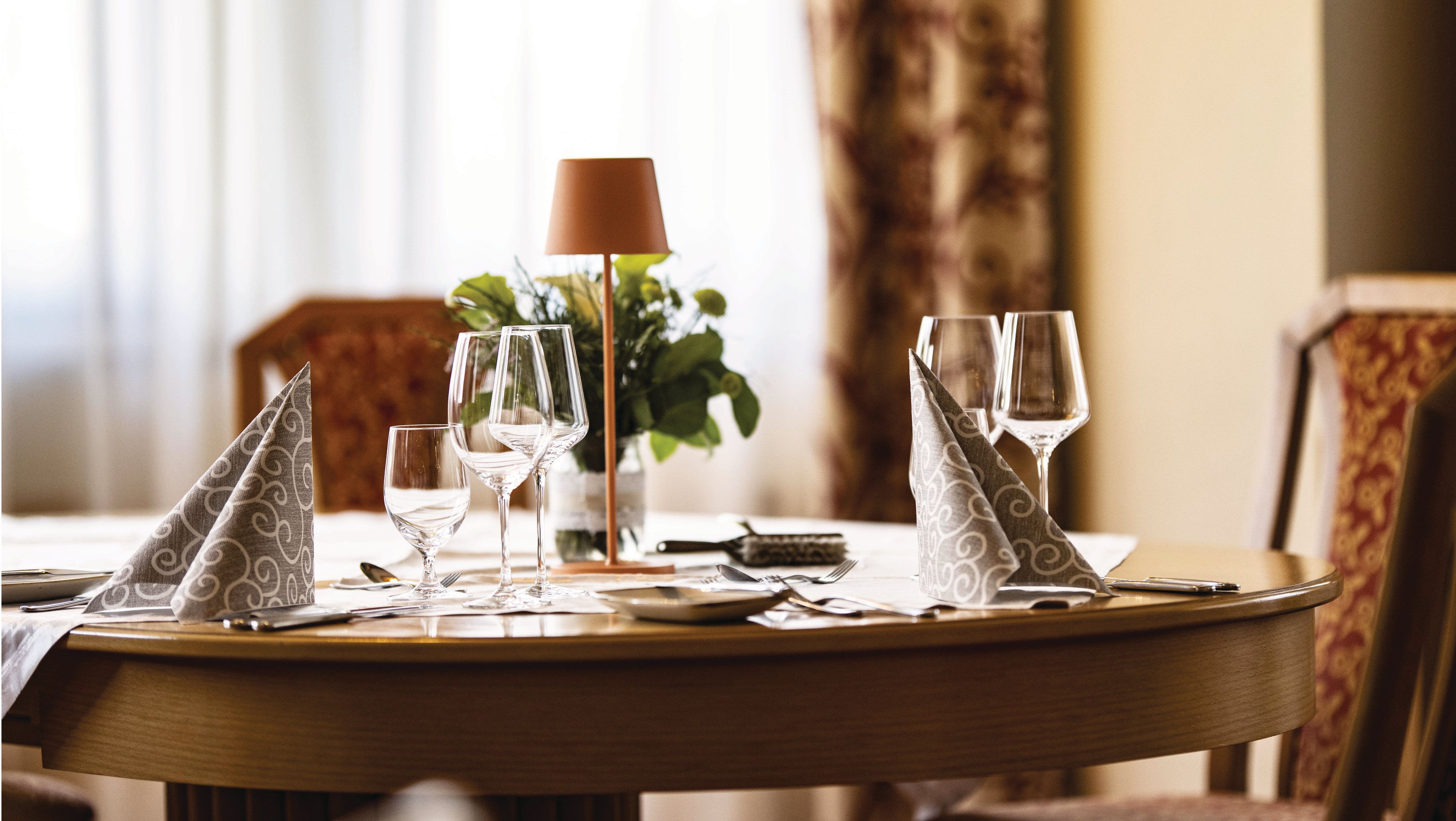 Eleganter Tisch im Restaurant mit Weingläsern, gefalteten Servietten und einer Pflanze als Dekoration.