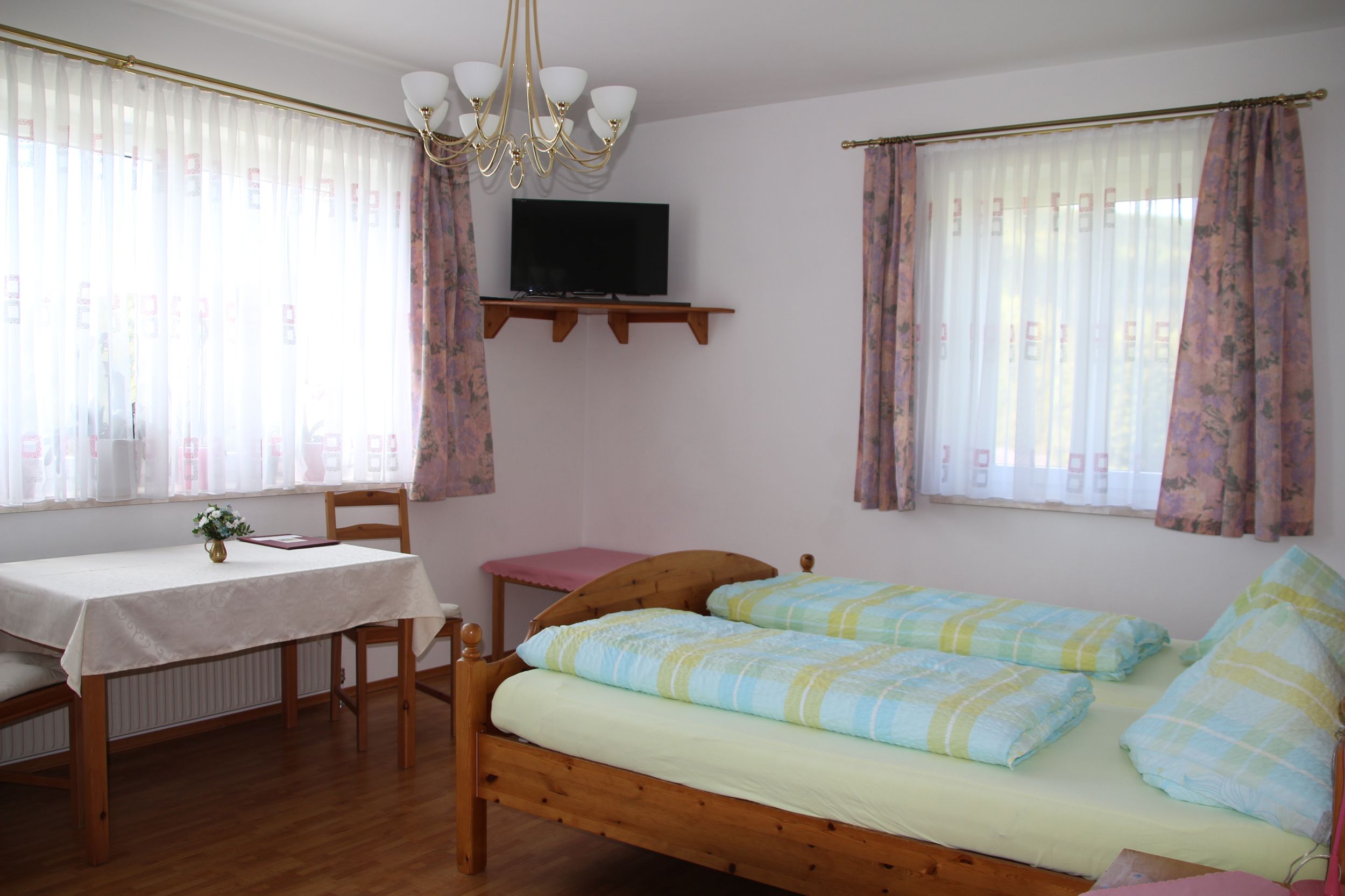 Ein helles Zimmer mit Doppelbett, Tisch, Stühlen und einem Fernseher an der Wand.