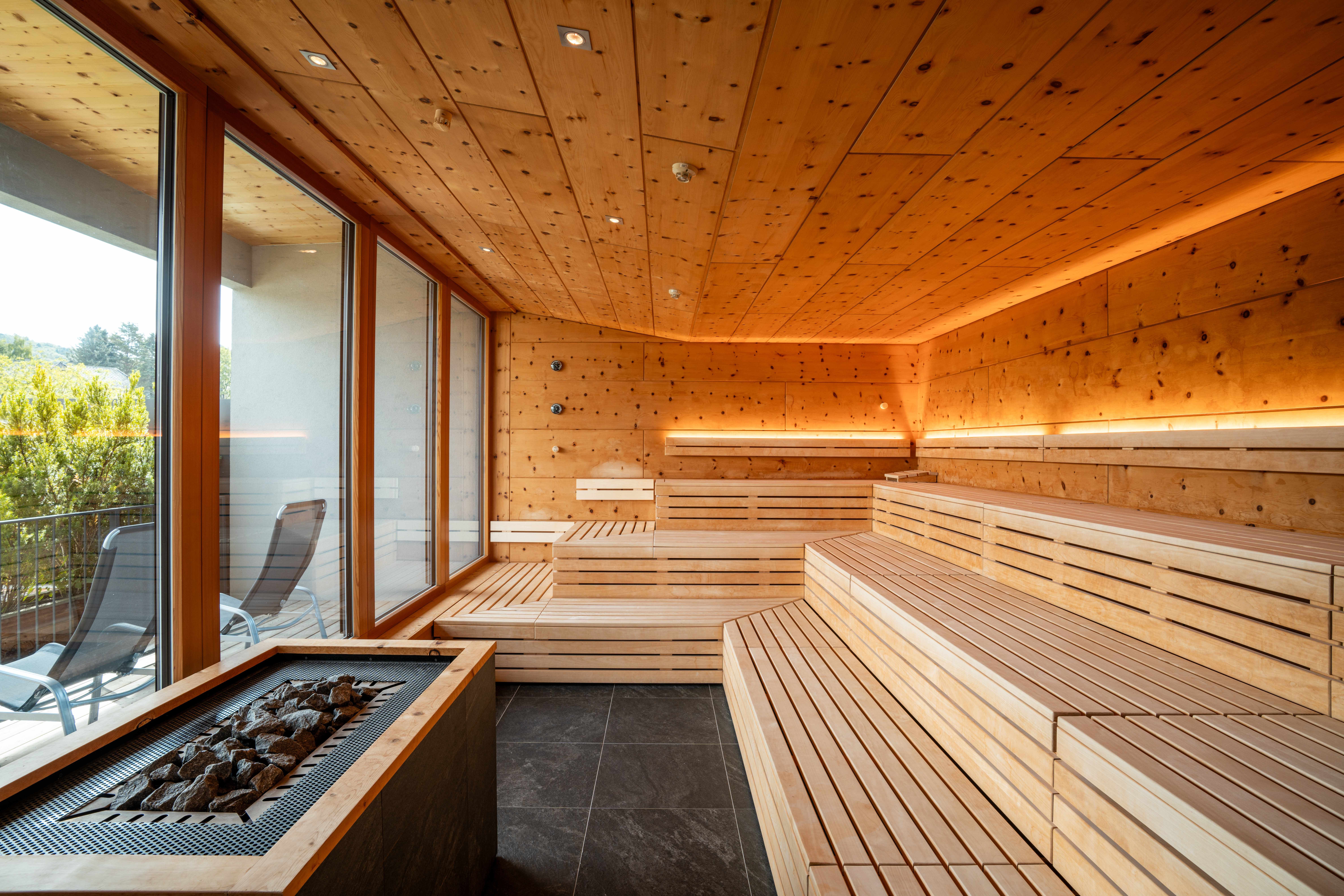 Innenansicht einer modernen Sauna mit Holzbänken und großen Fenstern.