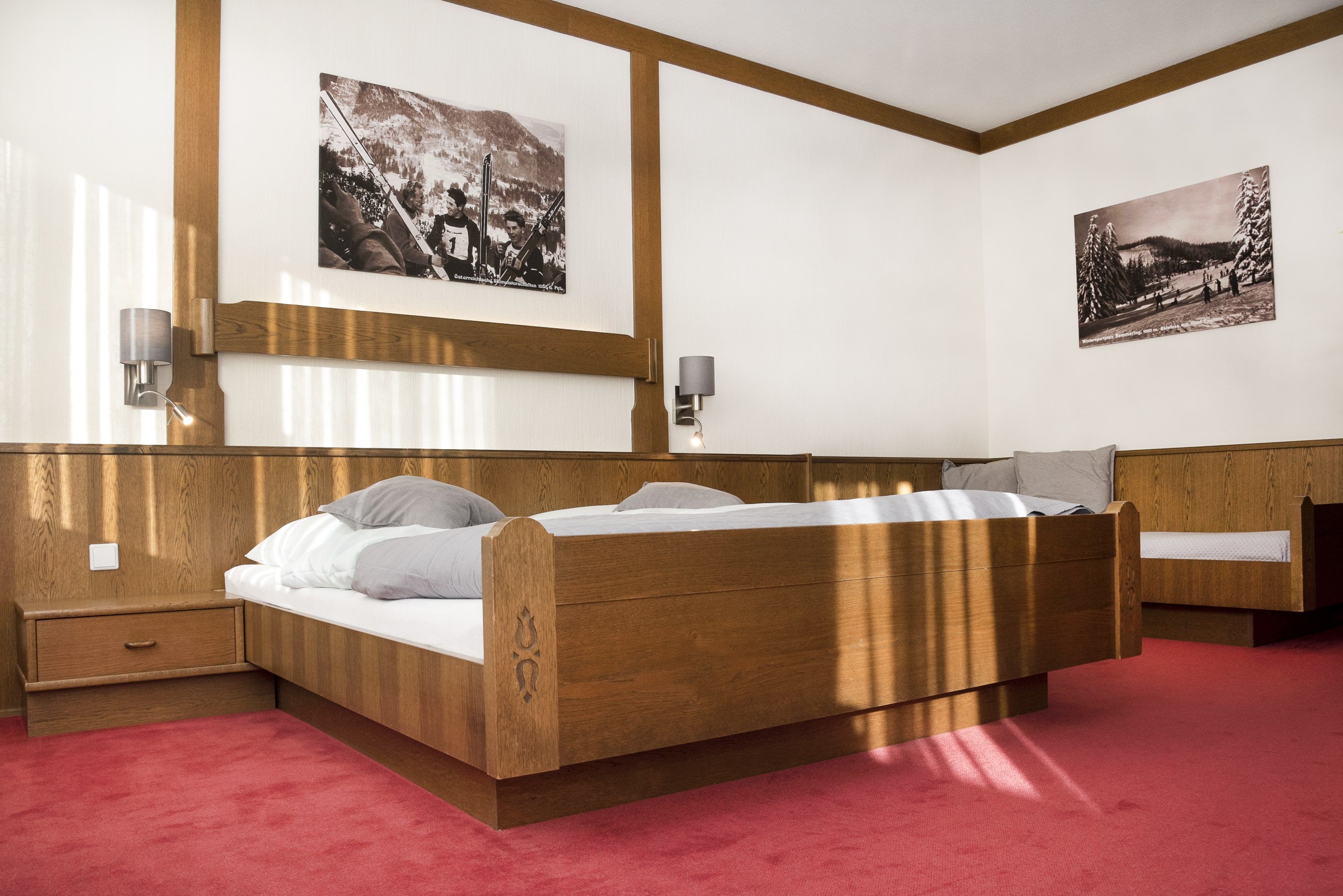 Ein Schlafzimmer mit einem hölzernen Doppelbett, rotem Teppichboden und zwei schwarz-weißen Bildern an der Wand.