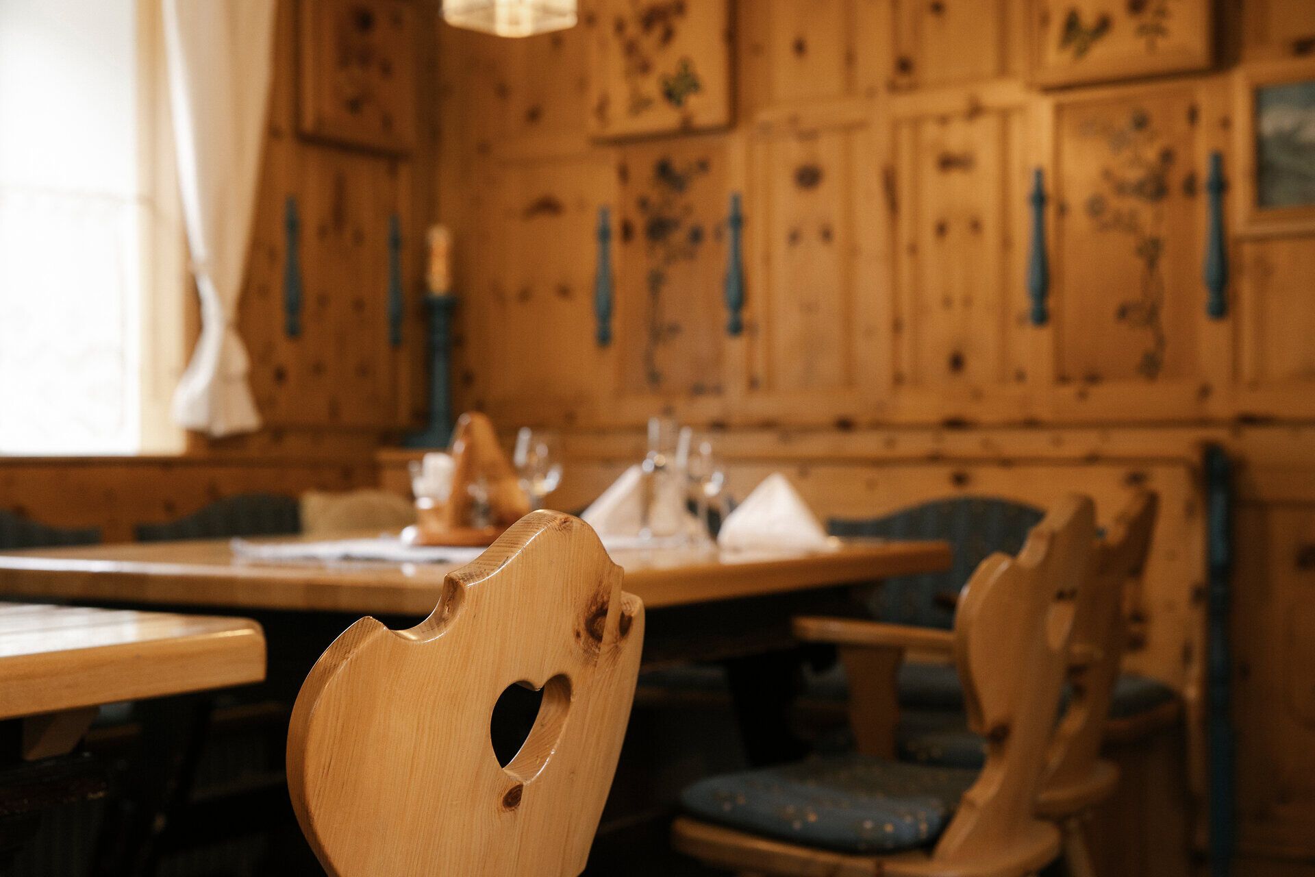 Gemütliche Stube mit Holzvertäfelungen, Tische und Stühle ebenfalls aus Holz mit blau bezogenen Sitzpolstern.