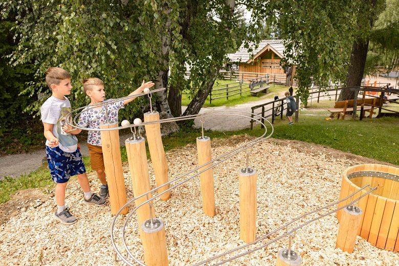 Zwei Kinder spielen an einer Kugelbahn im Freien.