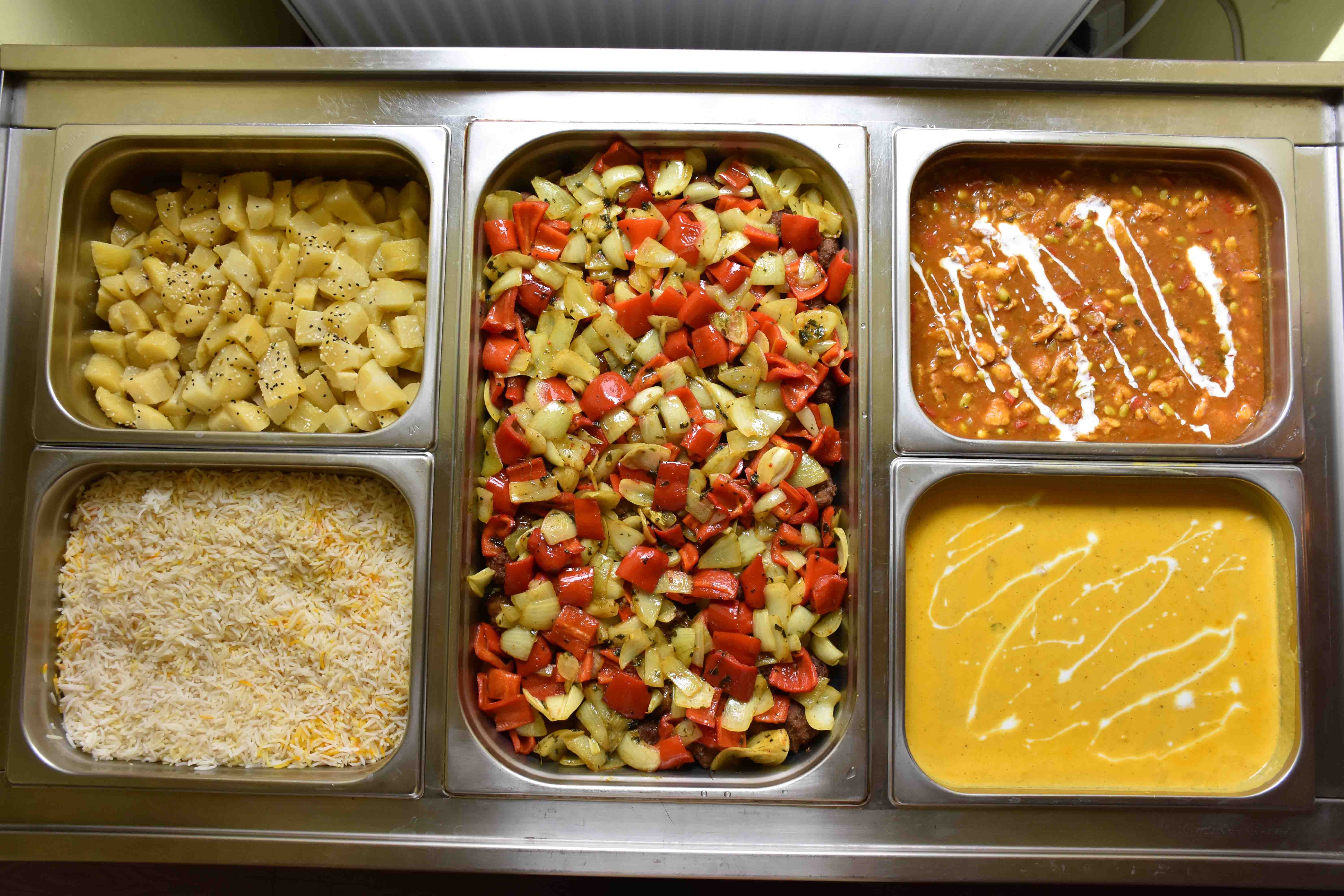 Verschiedene indische Gerichte in Metallbehältern. Unter anderem Reis, Kartoffeln, Gemüse und verschiedene Soßengerichte.