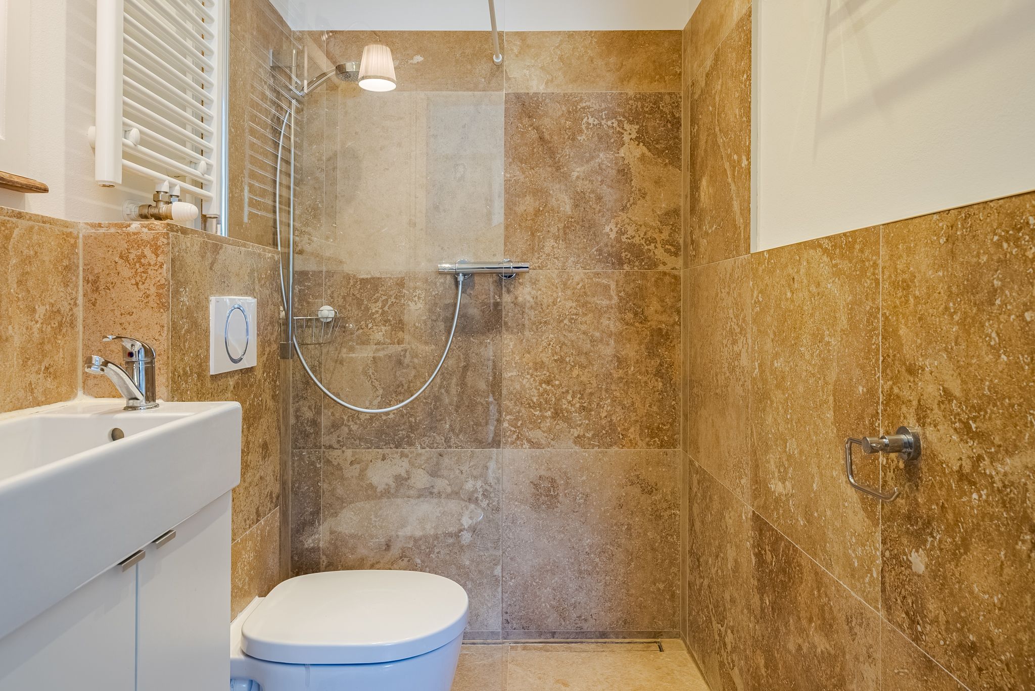 Modernes Badezimmer mit beigen Fliesen, Dusche, Waschbecken und Toilette.