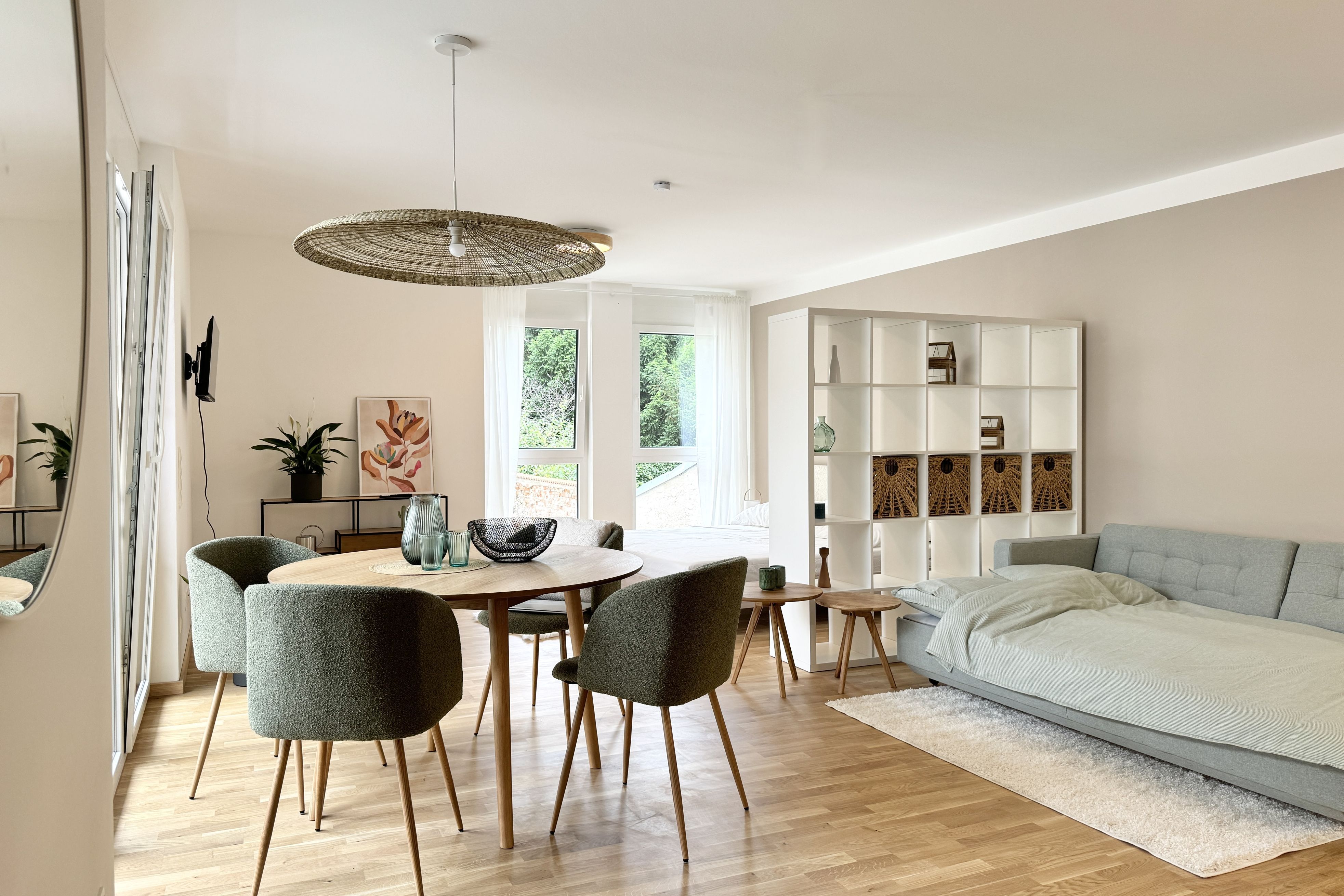 Helles Wohnzimmer mit grauer Couch, Raumteiler, Esstisch und beigen Wänden