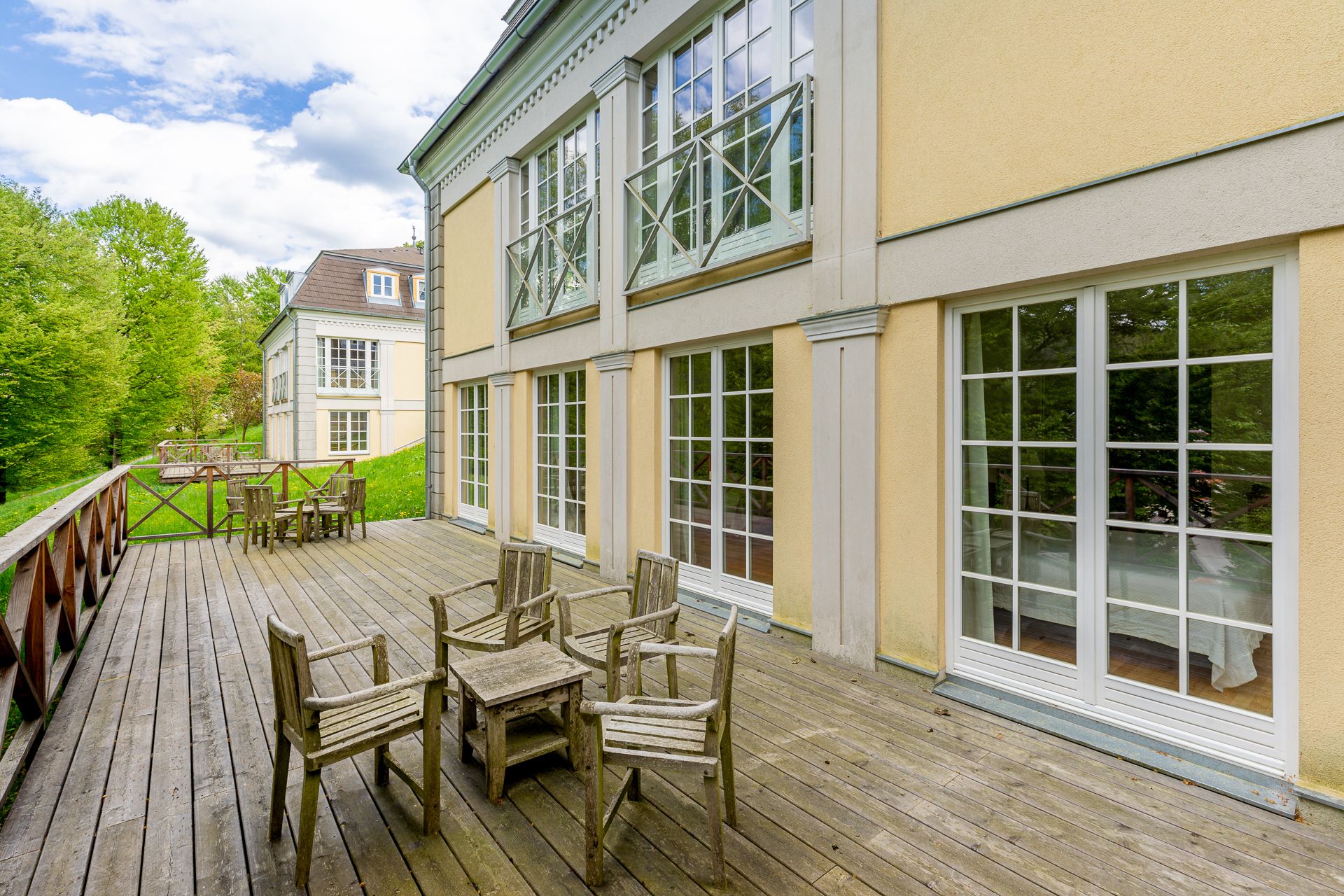 Holzterrasse mit Stühlen vor gelbem Gebäude mit großen Fenstern.