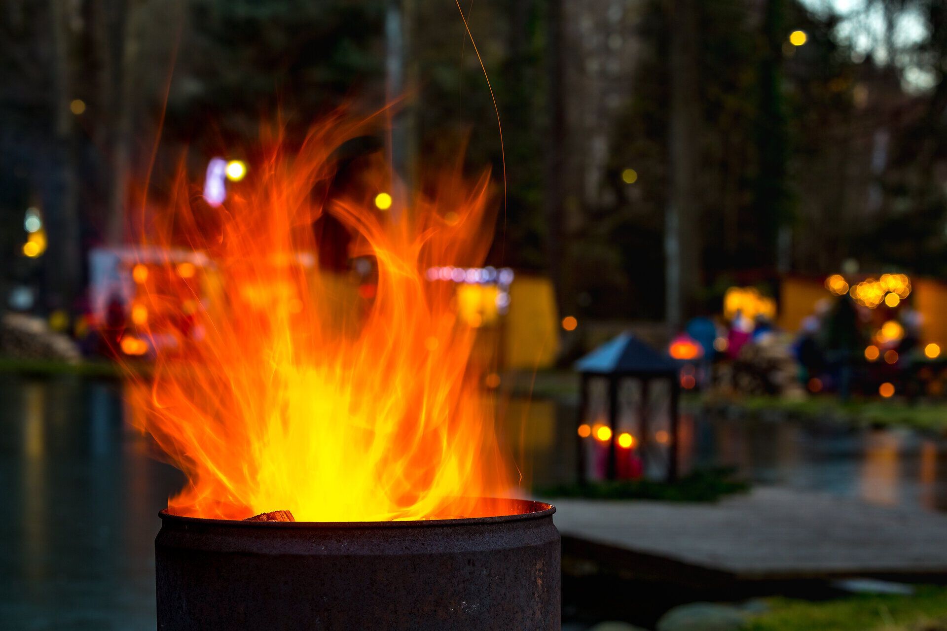 Flammen einer Feuerschale vor einem stimmungsvoll beleuchteten Adventmarkt am Wasser.