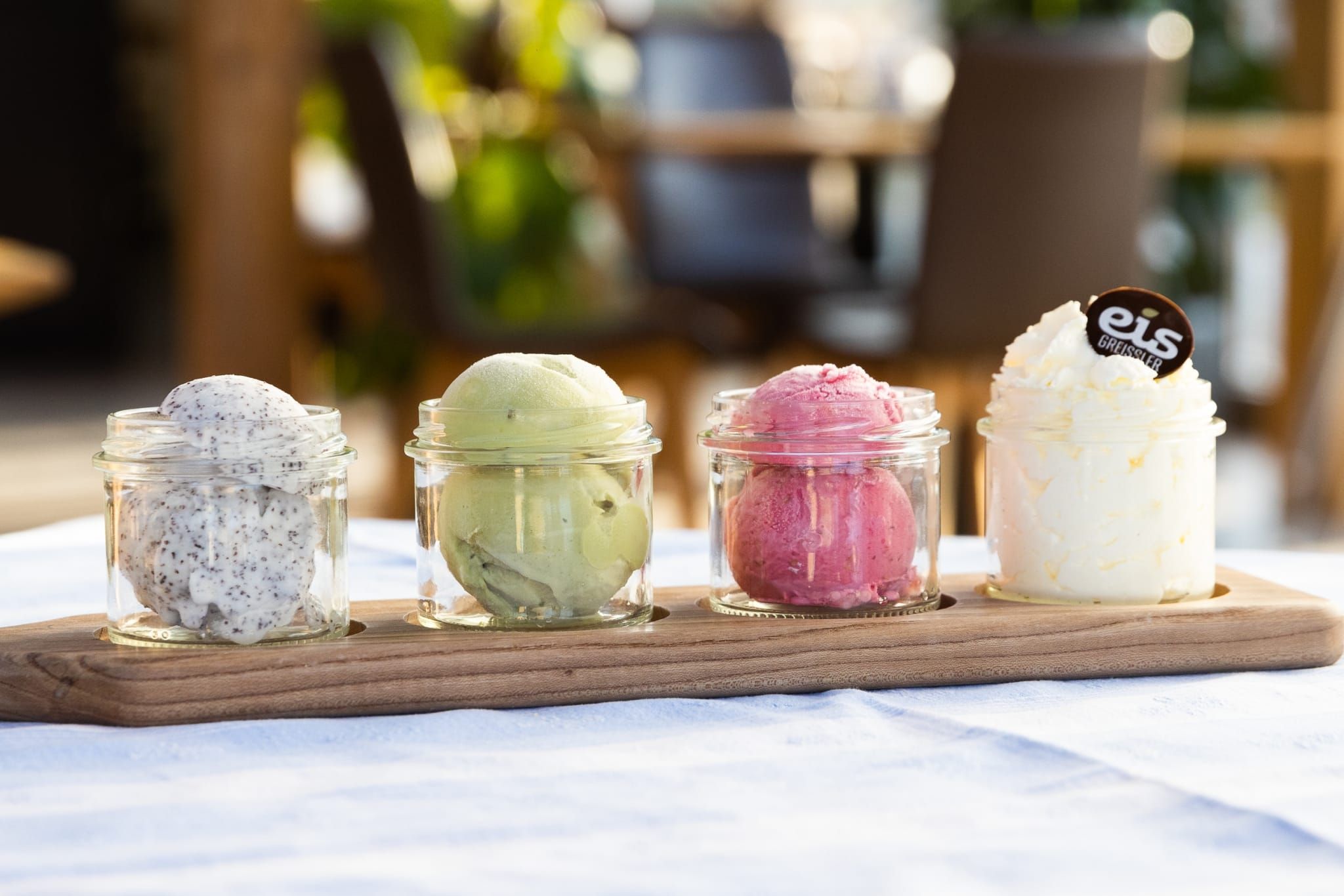 Ein Holzbrett mit vier Gläsern mit jeweils einer Kugel Eis unterschiedlicher Sorten.