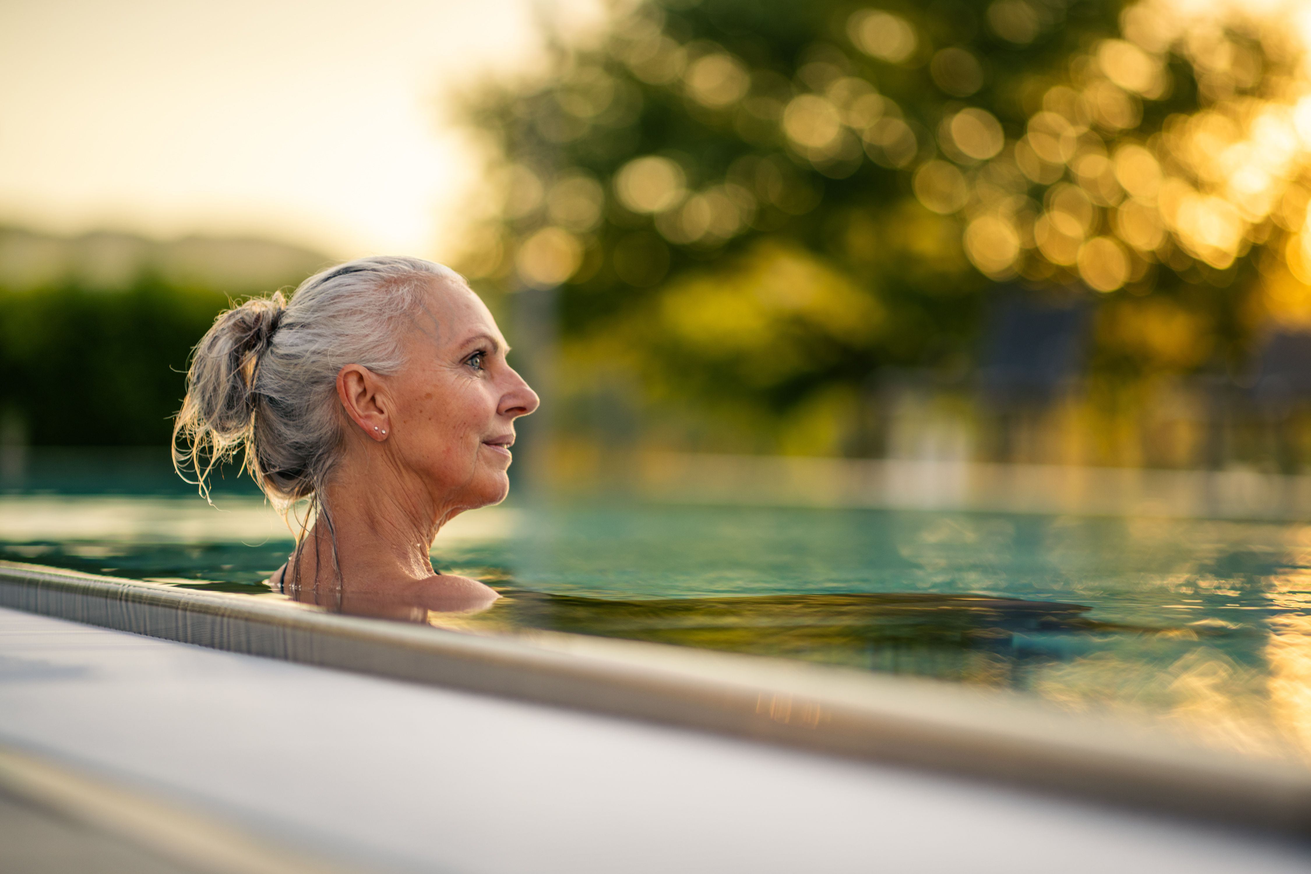 Eine ältere Frau genießt ein Bad in einem Pool bei Sonnenuntergang.