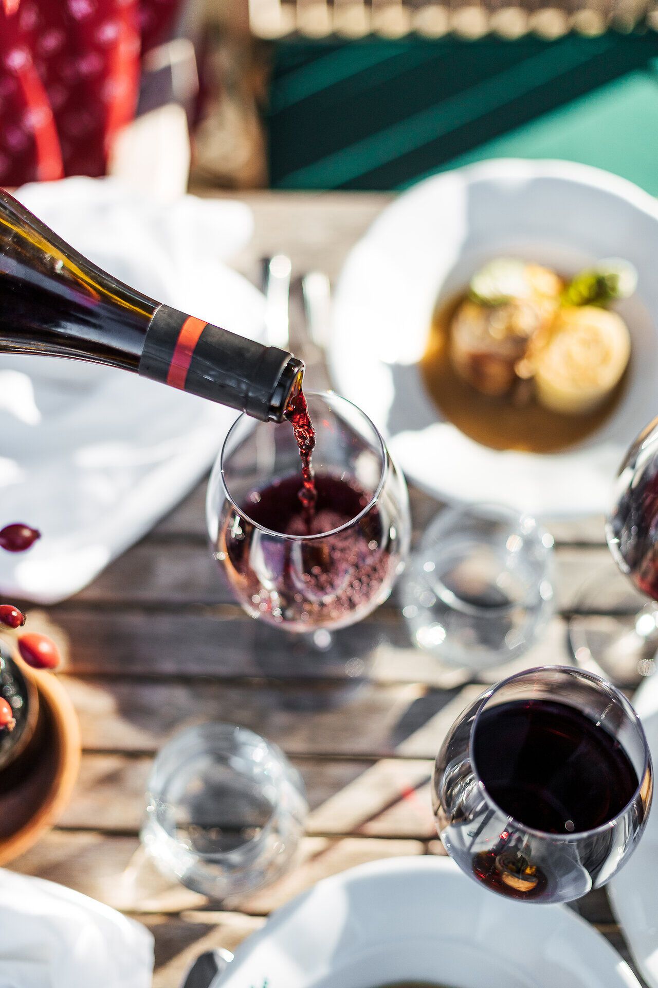 Ein köstlicher Rotwein fließt sanft in ein elegantes Glas, während die Sonne sanft über die malerische Landschaft der Wiener Alpen strahlt. Die Atmosphäre ist entspannt und einladend, perfekt für einen genussvollen Abend inmitten der Natur.