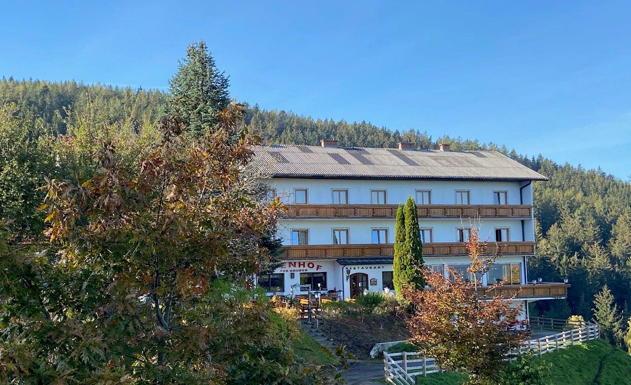 Gasthof-Pension Ödenhof vor einem bewaldeten Hügel.