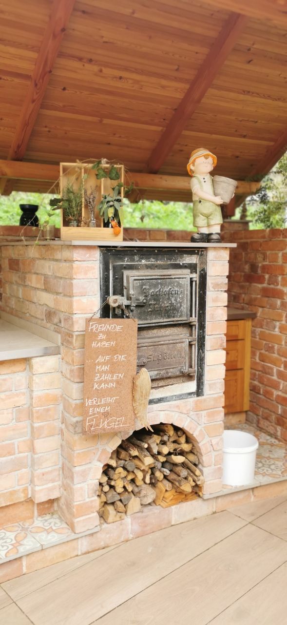 Backofen aus Ziegelsteinen mit Holzlagerung und Dekorationen unter einem Holzdach.