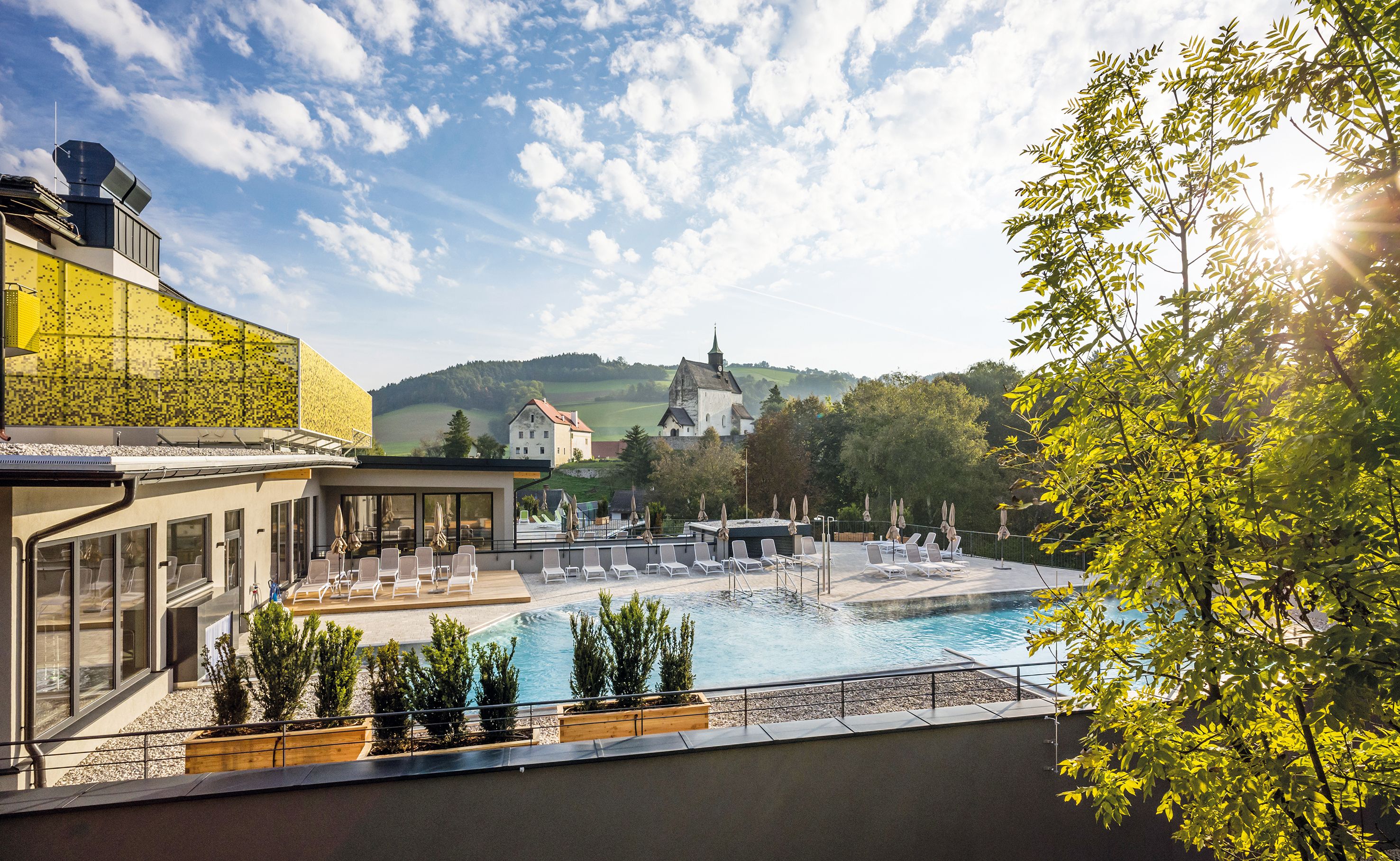 Einladend strahlt der Außenpool des Resorts in der warmen Sonne, umgeben von üppigem Grün und sanften Hügeln. Die ruhige Atmosphäre lädt dazu ein, die Seele baumeln zu lassen und die Schönheit der Natur zu genießen.