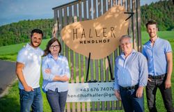 Vier Personen stehen vor einer Holztafel mit der Aufschrift 'Haller Hendlhof' im Freien.