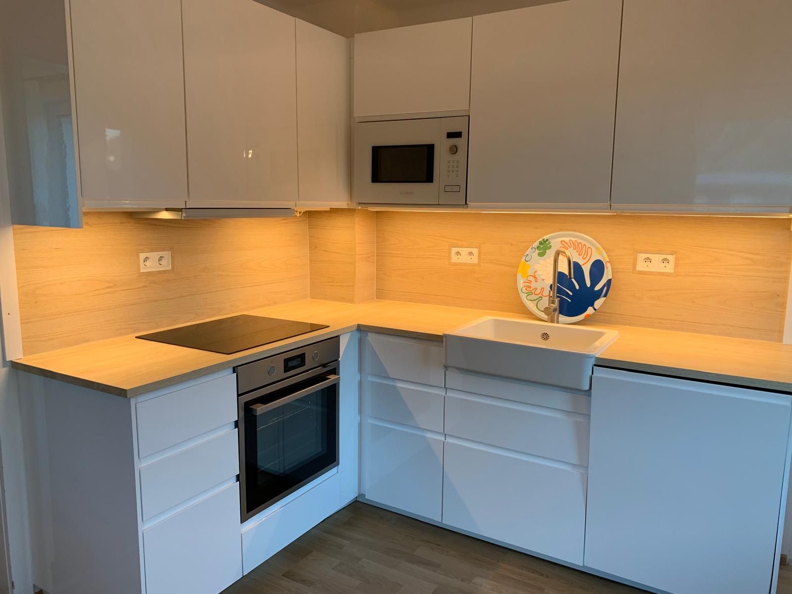 Moderne Küche mit weißen Schränken, Holzarbeitsplatte, eingebautem Ofen und Spüle.