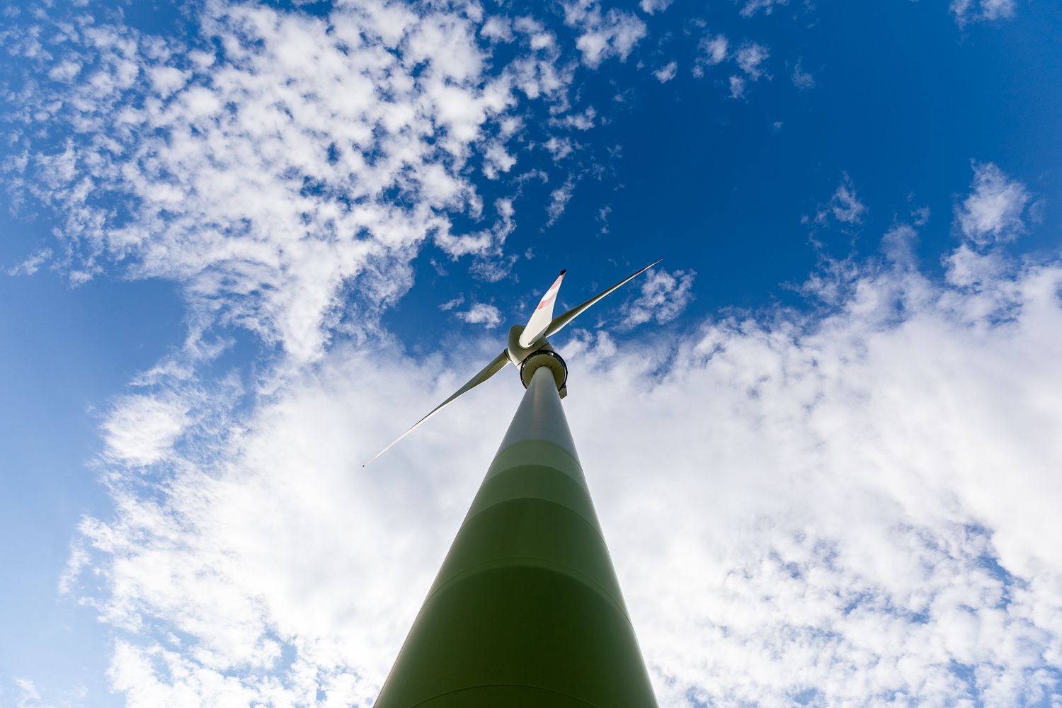 Blick von unten auf ein Windrad vor blauem Himmel mit Wolken.