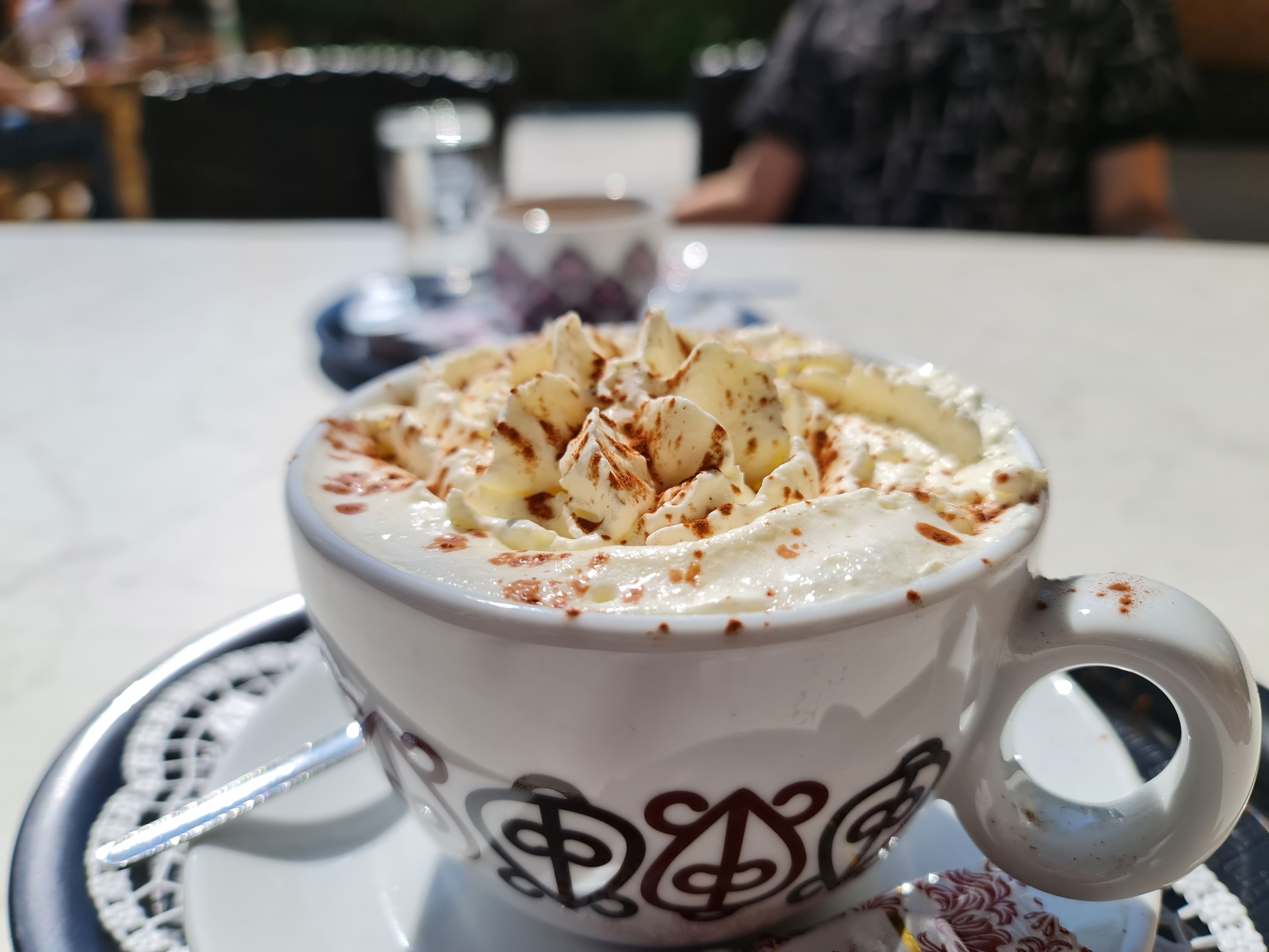 Nahaufnahme einer Tasse heiße Schokolade mit Sahne und Kakaopulver auf einem Tisch im Freien.