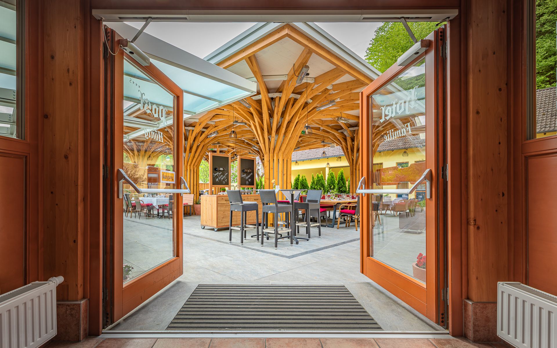 Offene Glastüren führen zu einer Terrasse mit Holzdach und Sitzgelegenheiten.