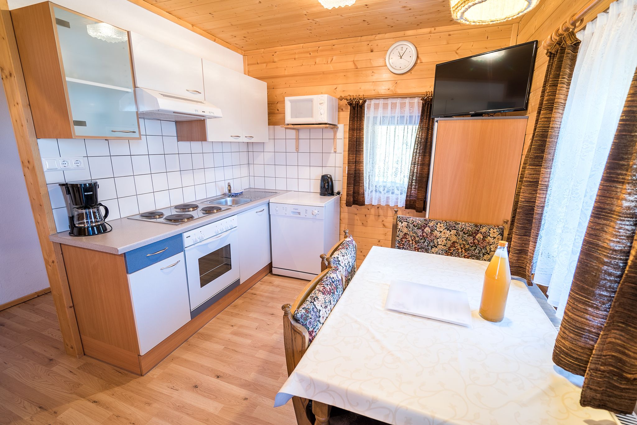 Gemütliche Küche mit Holzwänden, Esstisch, Herd, Kaffeemaschine und Fernseher.