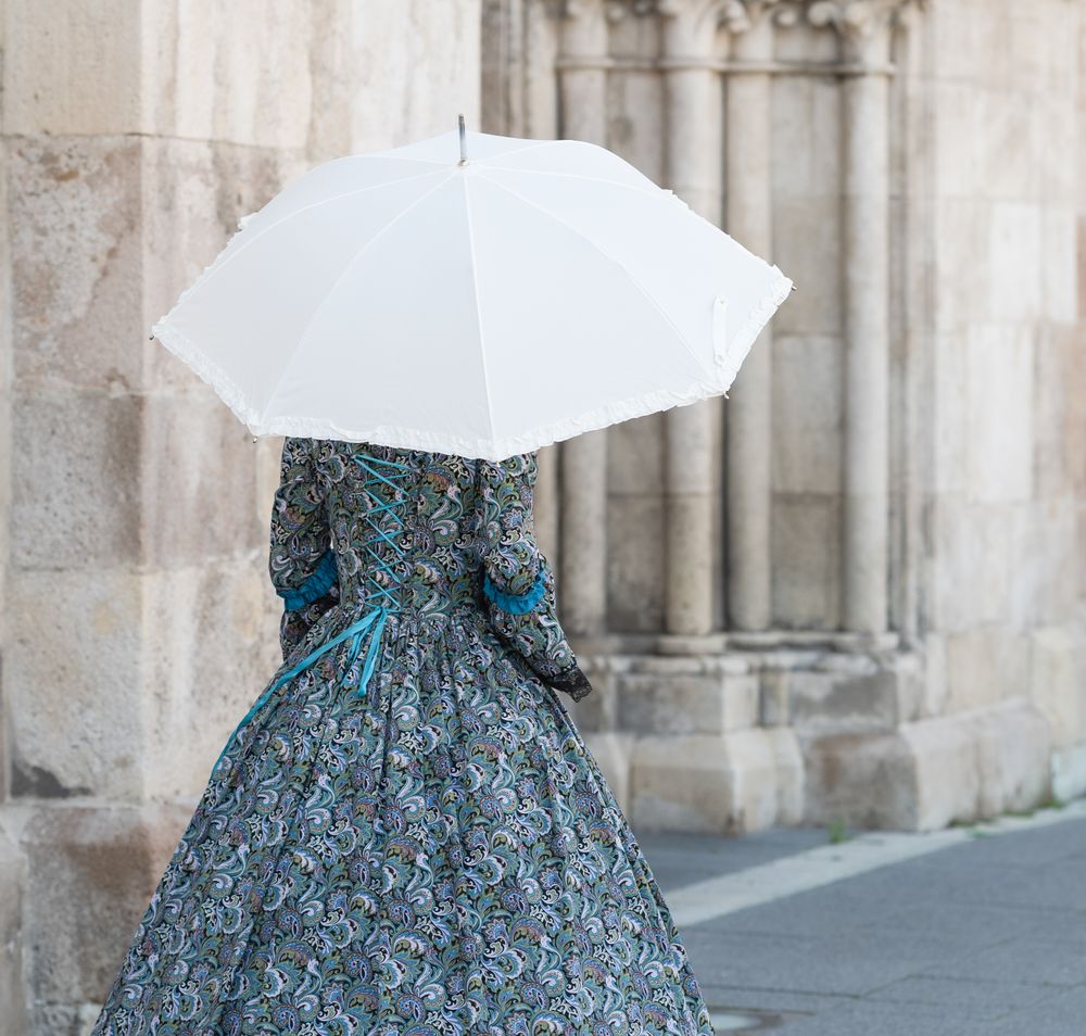 Historisch gekleidete Frau mit Kleid und Sonnenschirm vor dem Dom. 