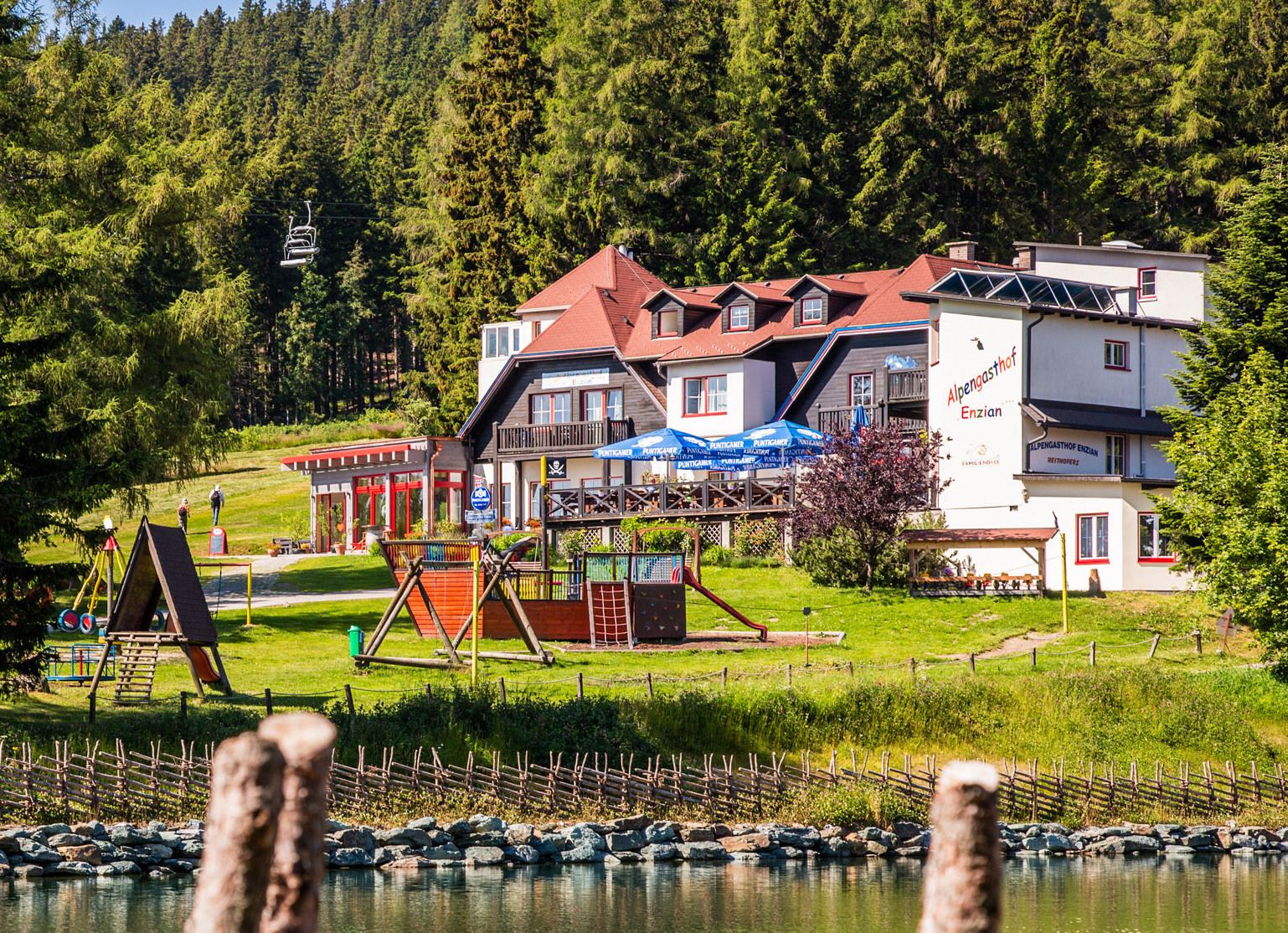 Alpengasthof Enzian mit Spielplatz und Wald im Hintergrund.
