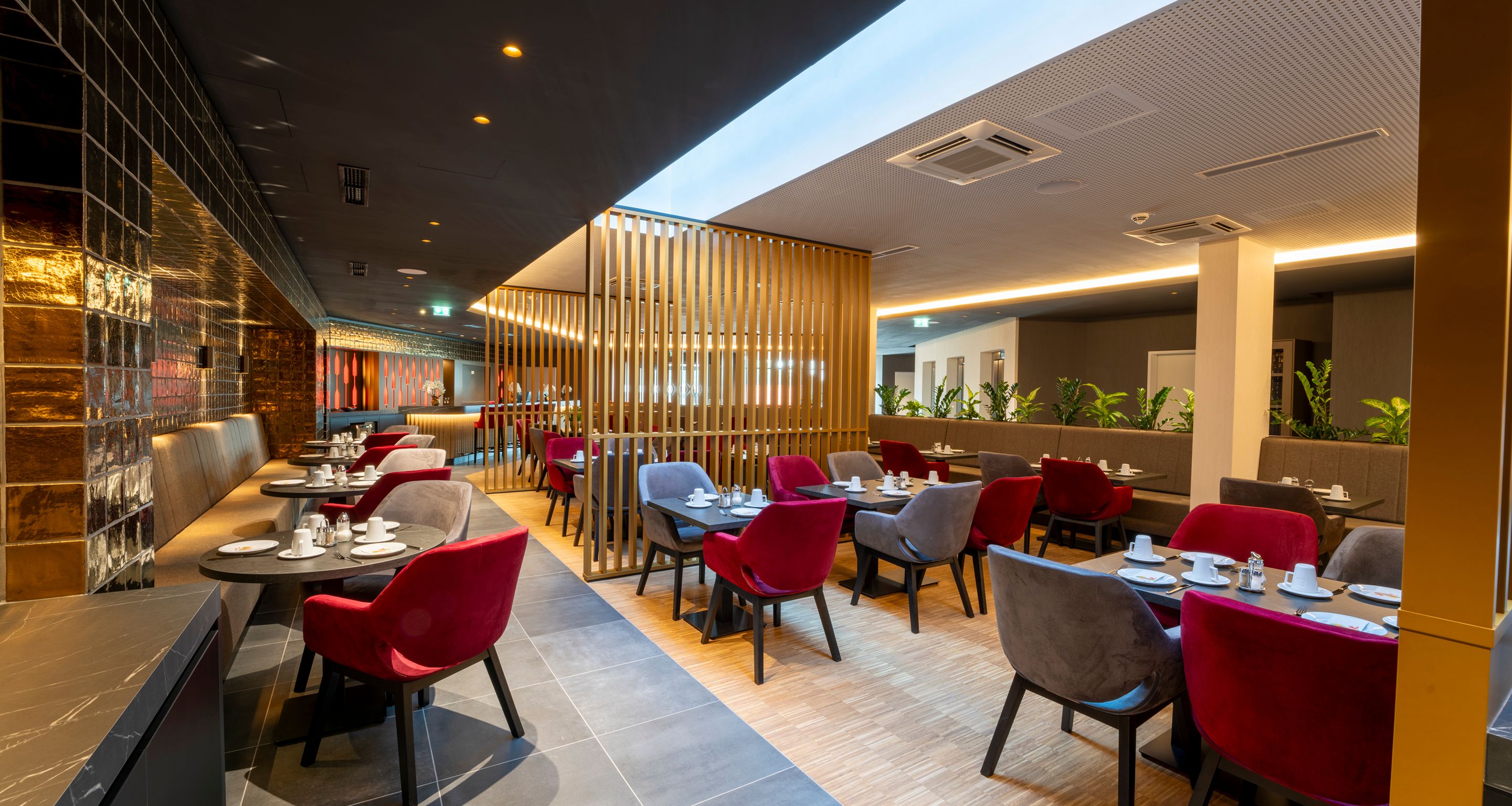 Modernes Hotelzimmer mit Doppelbett, roten Sesseln und großen Fenstern mit Vorhängen.