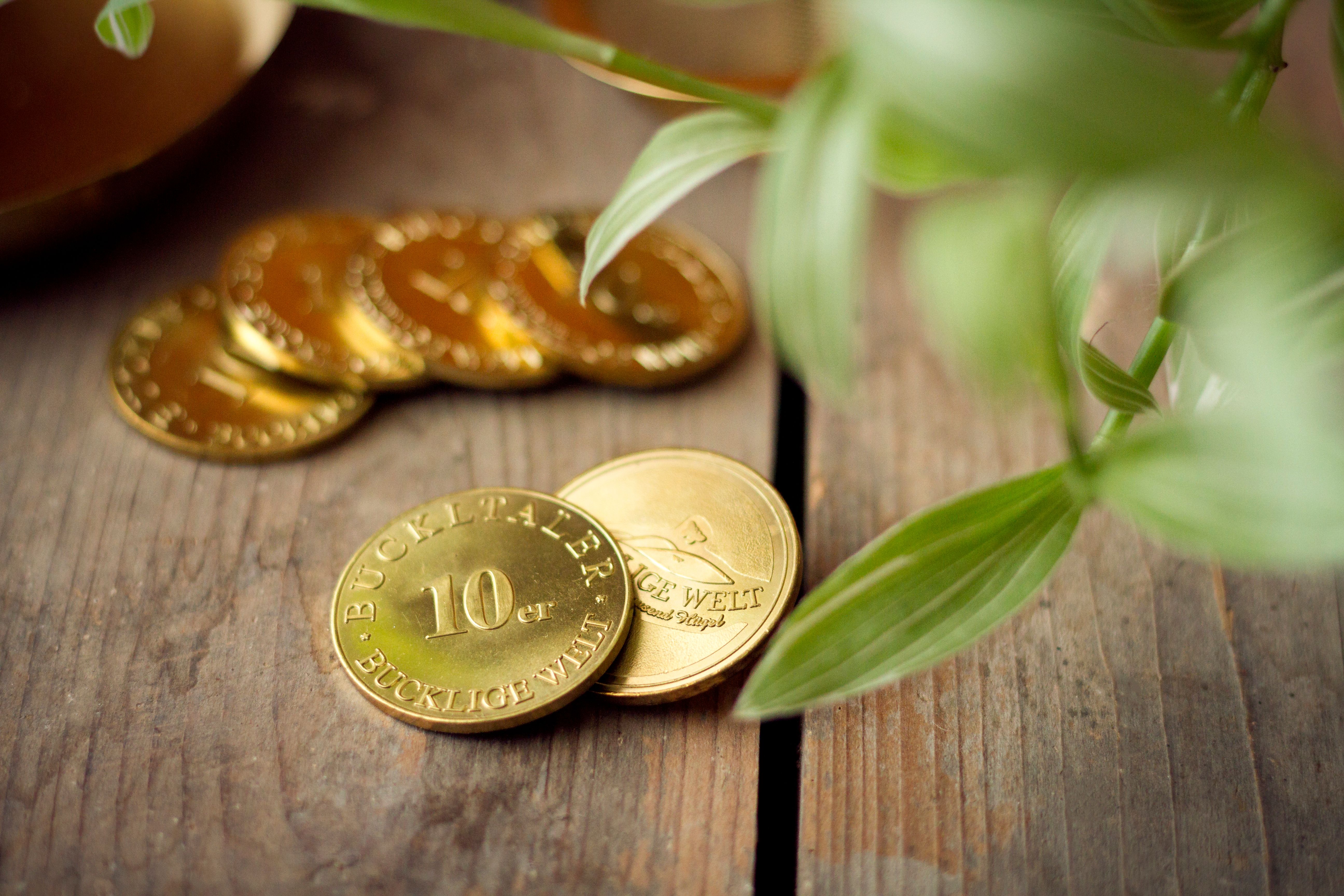Goldene Buckeltaler-Münzen auf Holzboden, daneben Blätter.