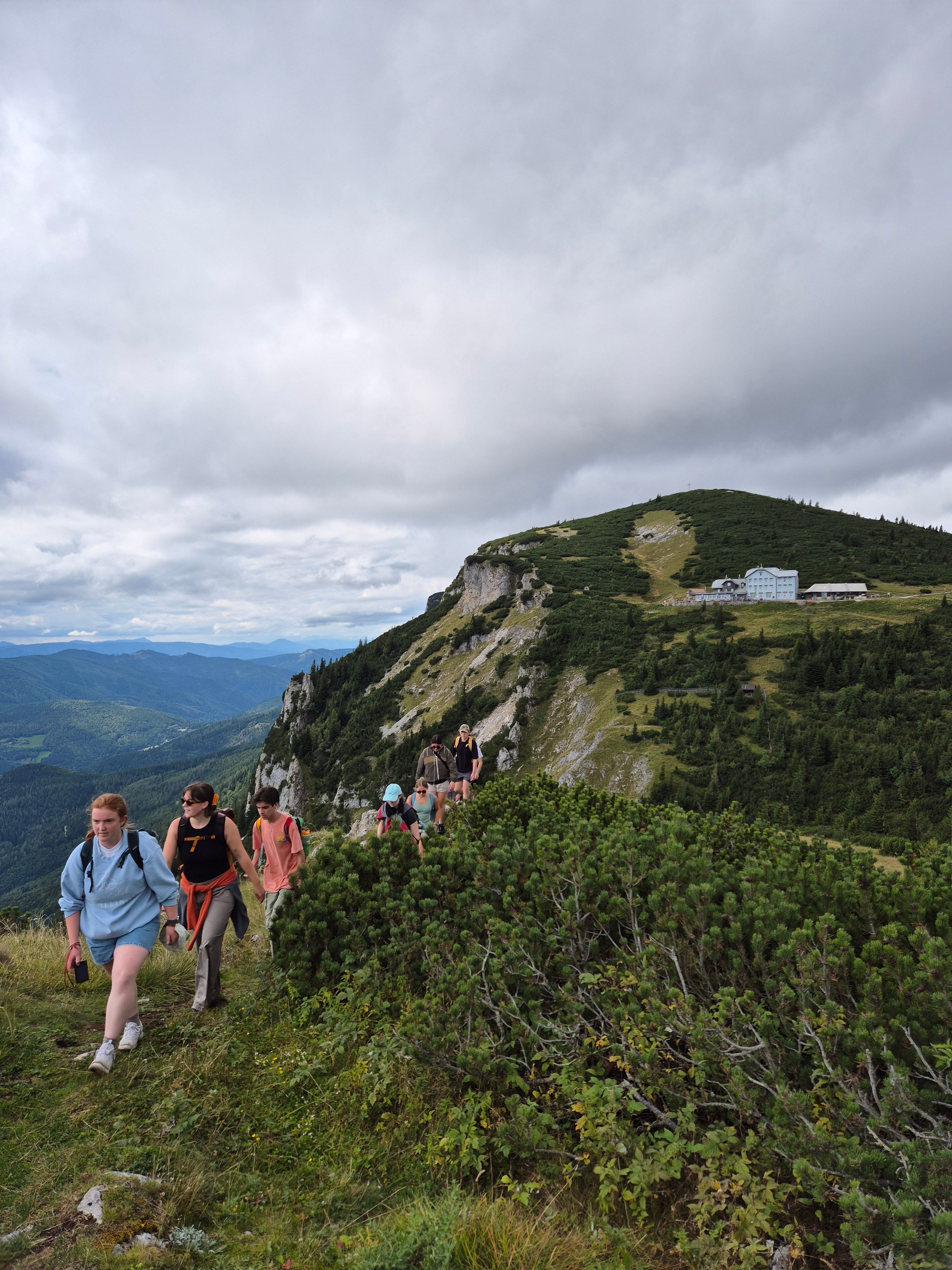 Gruppe von Wanderern auf einem Bergpfad mit bewölktem Himmel.