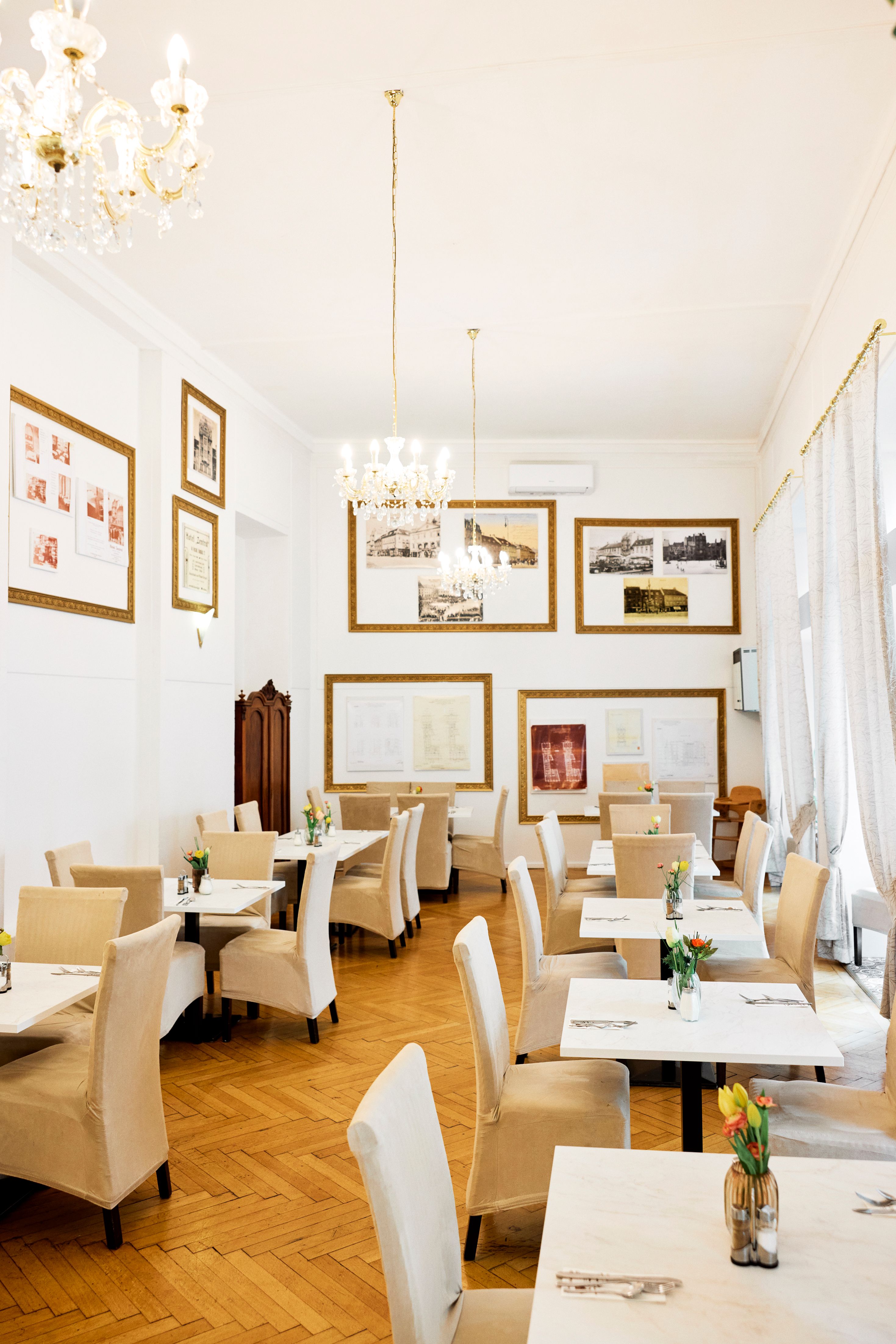Großes, helles Restaurant mit beigen Möbeln, hohen Wänden und Bildern an der Wand