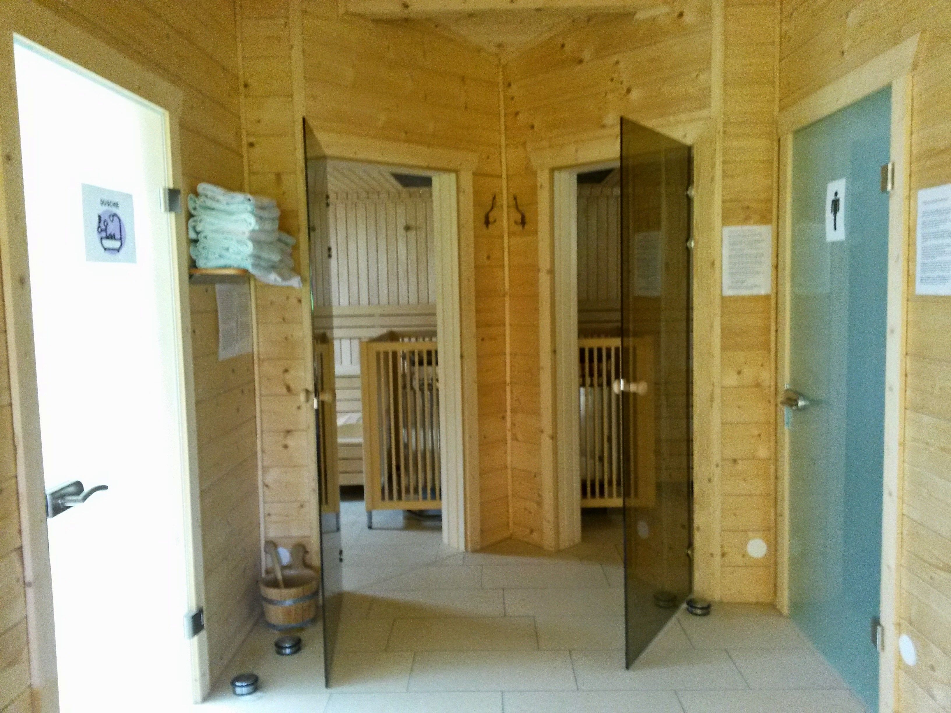 Innenansicht einer Sauna mit Holzwänden, Glastüren und Handtüchern.