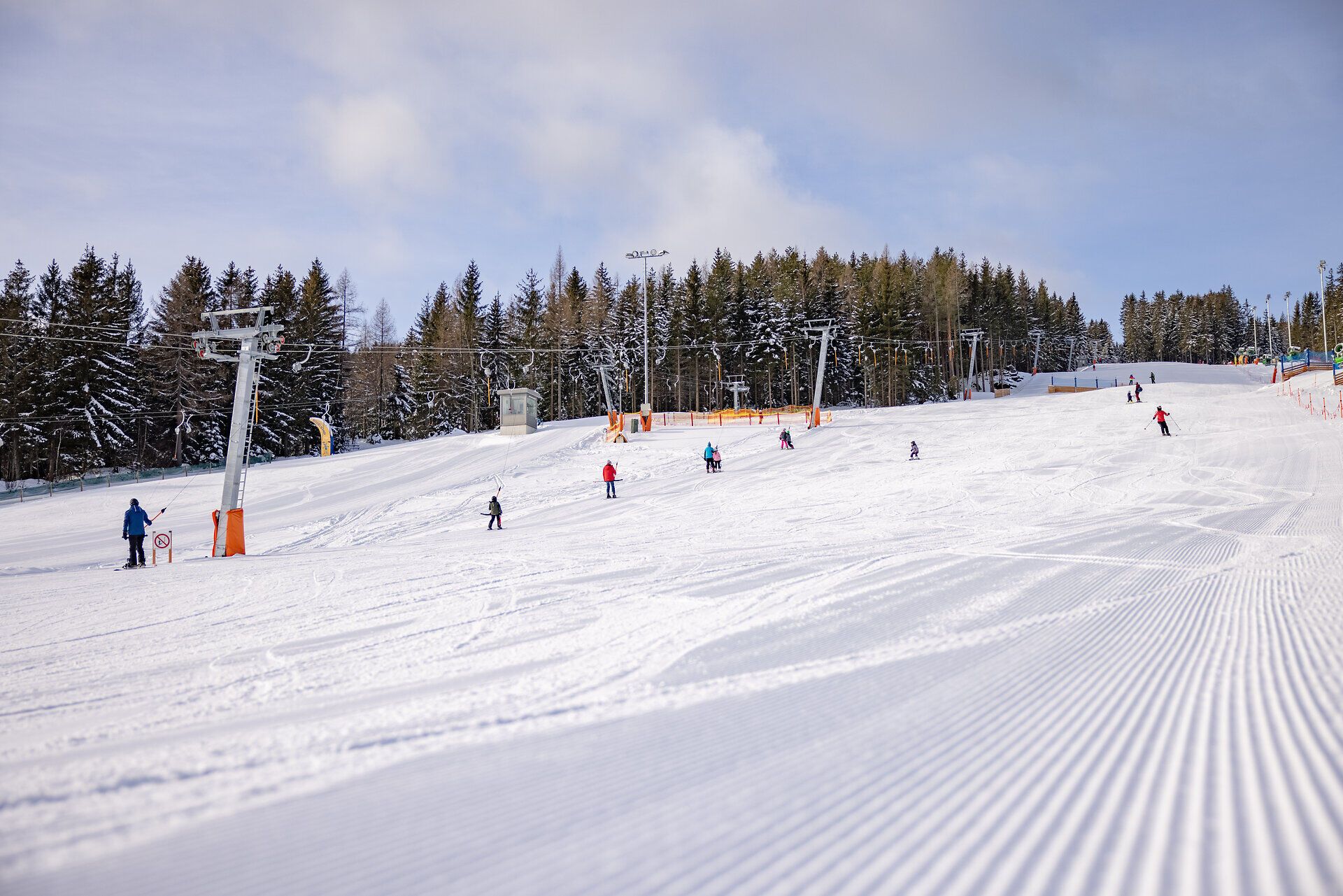 Kinder und Erwachsene beim Skifahren auf den breiten Pisten im Kinderskiland der Wexl Arena