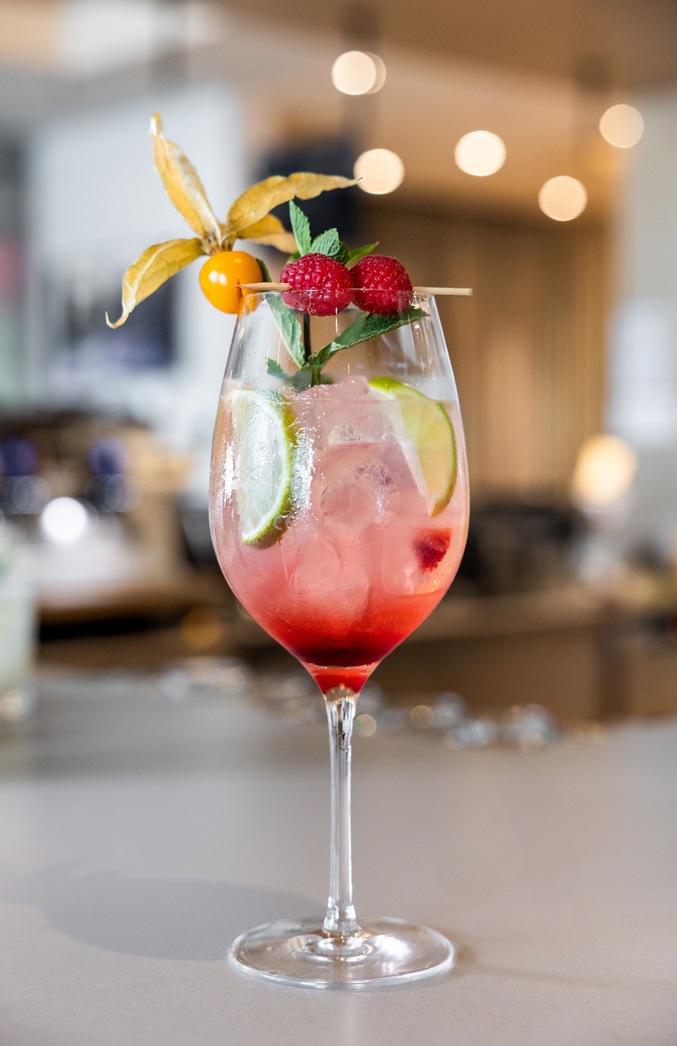 Roter Drink im Sektglas, garniert mit Himbeeren, Limetten und Physalis