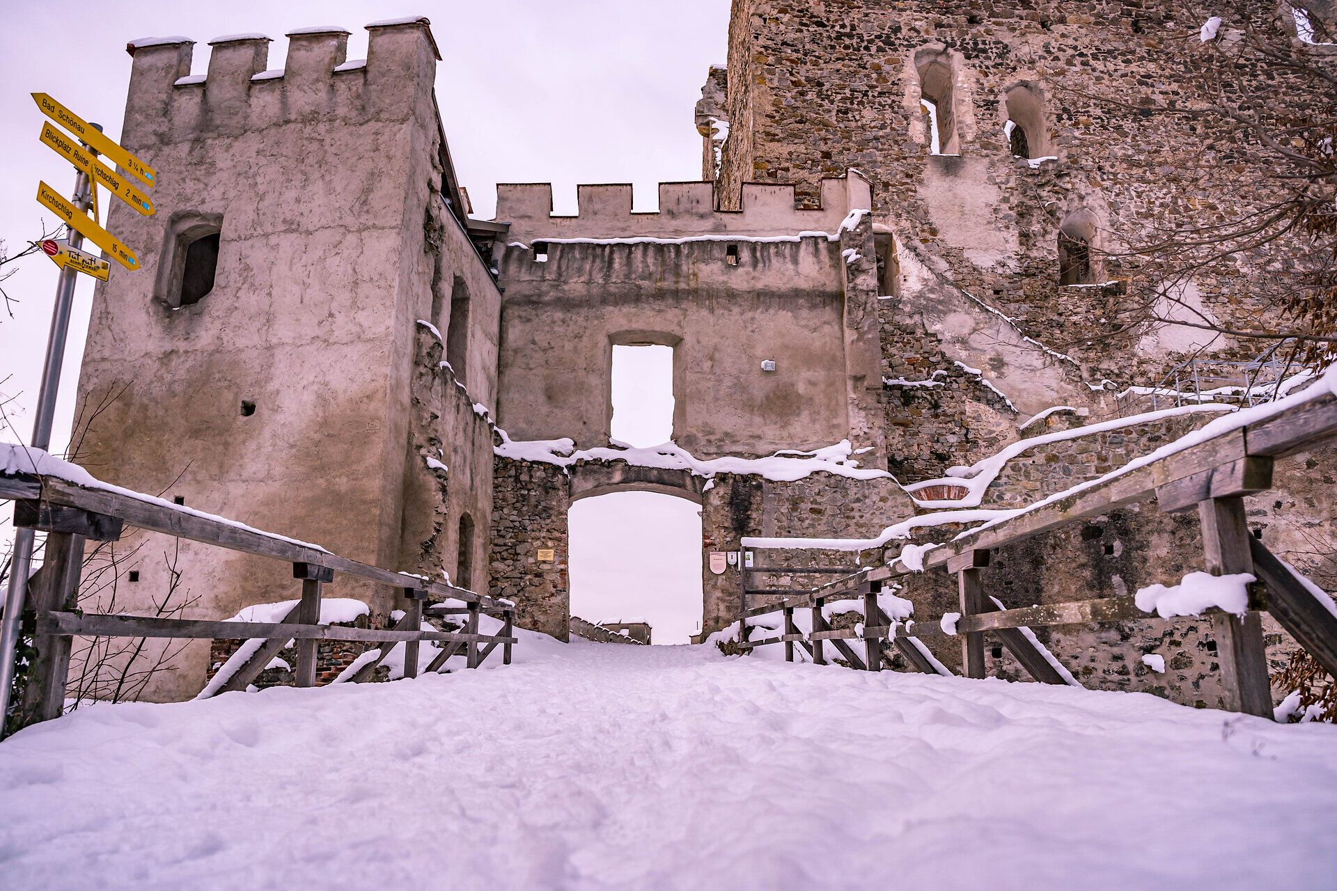 Die Brücke zum Burgtor der Burgruine Kirchschlag sowie das Geländer sind mit einer Schneeschicht bedeckt. 