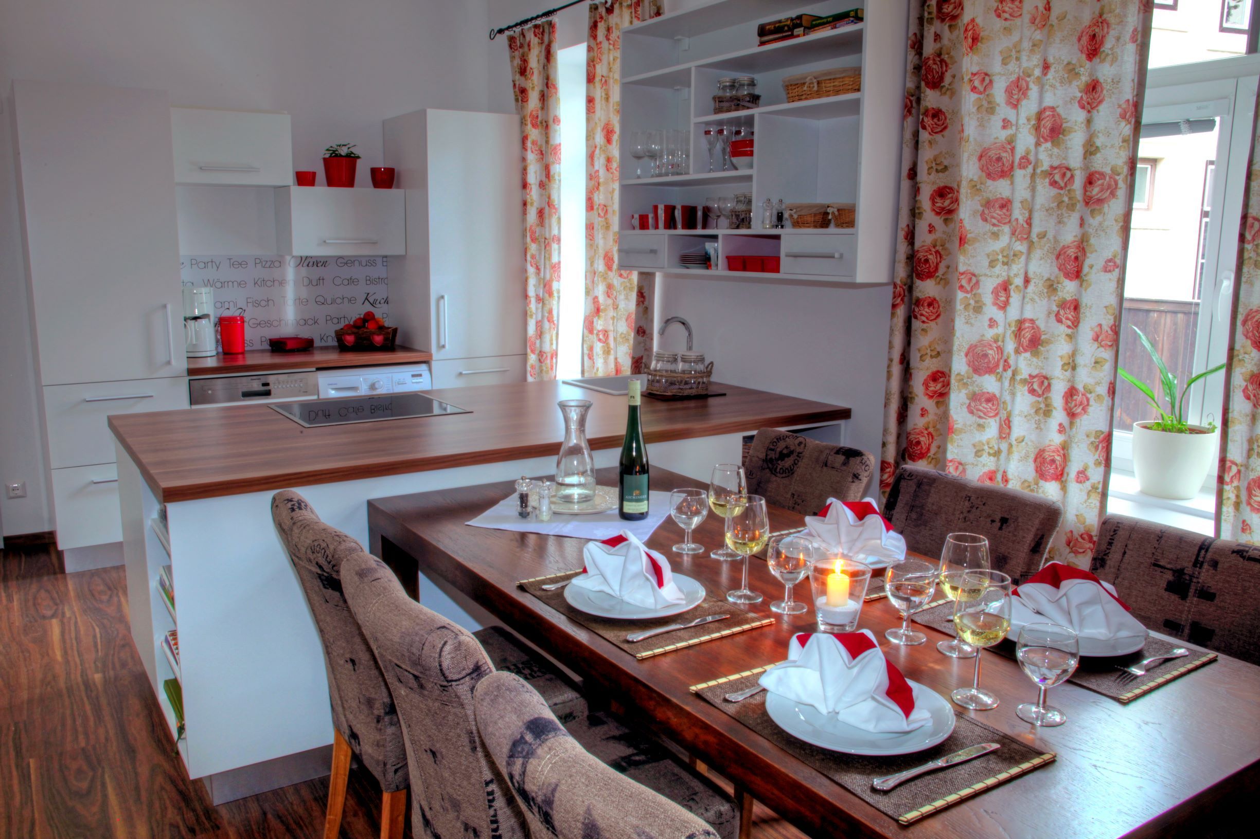 Moderne Küche mit Esstisch, gedeckt mit Gläsern und Servietten, Blumenmuster-Vorhänge.