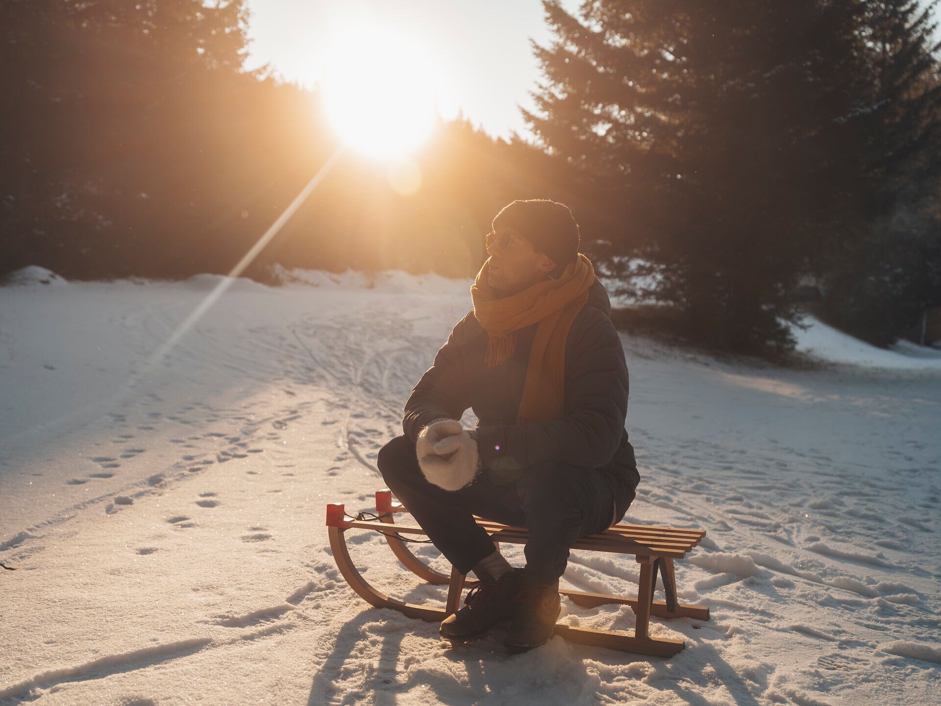 In der winterlichen Landschaft der Wiener Alpen sitzt ein Mann auf einer Rodel und genießt die warmen Sonnenstrahlen, die durch die Bäume scheinen. Der glitzernde Schnee und die ruhige Umgebung laden zu einem unvergesslichen Tag im Freien ein, während die frische Bergluft die Sinne belebt.
