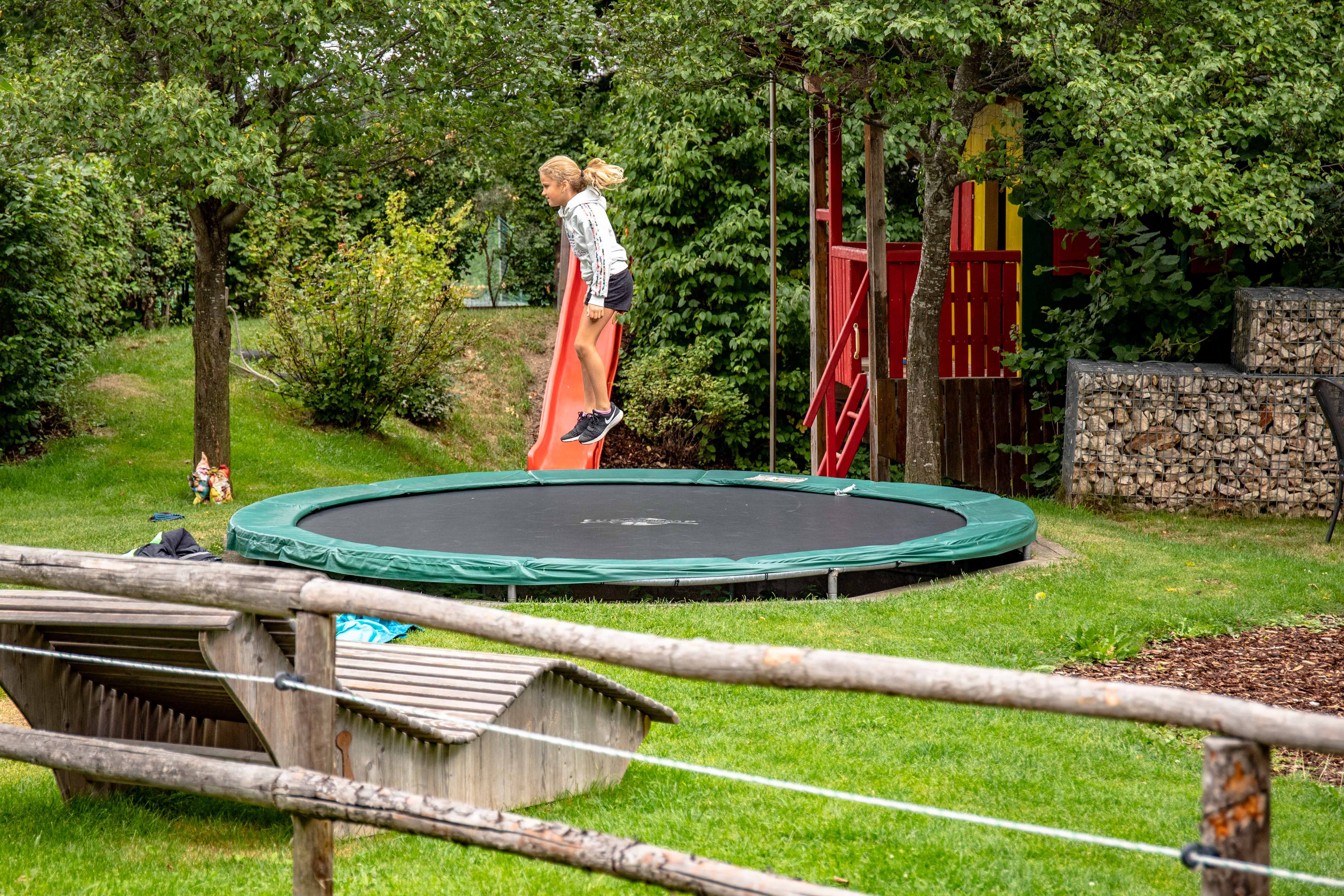 Ein Kind springt auf einem Trampolin in einem Garten mit Rutsche und Spielhaus.