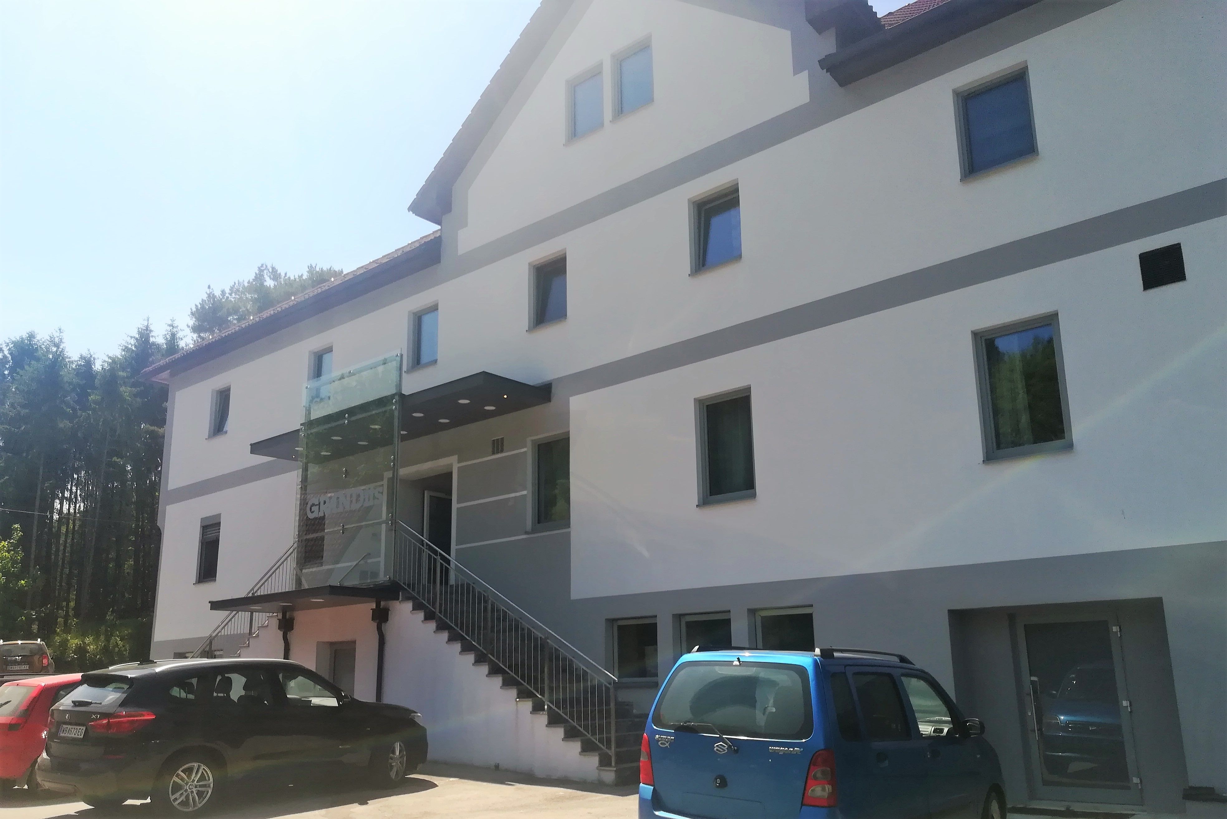 Außenansicht eines modernen Gasthauses mit mehreren Fenstern und parkenden Autos davor.