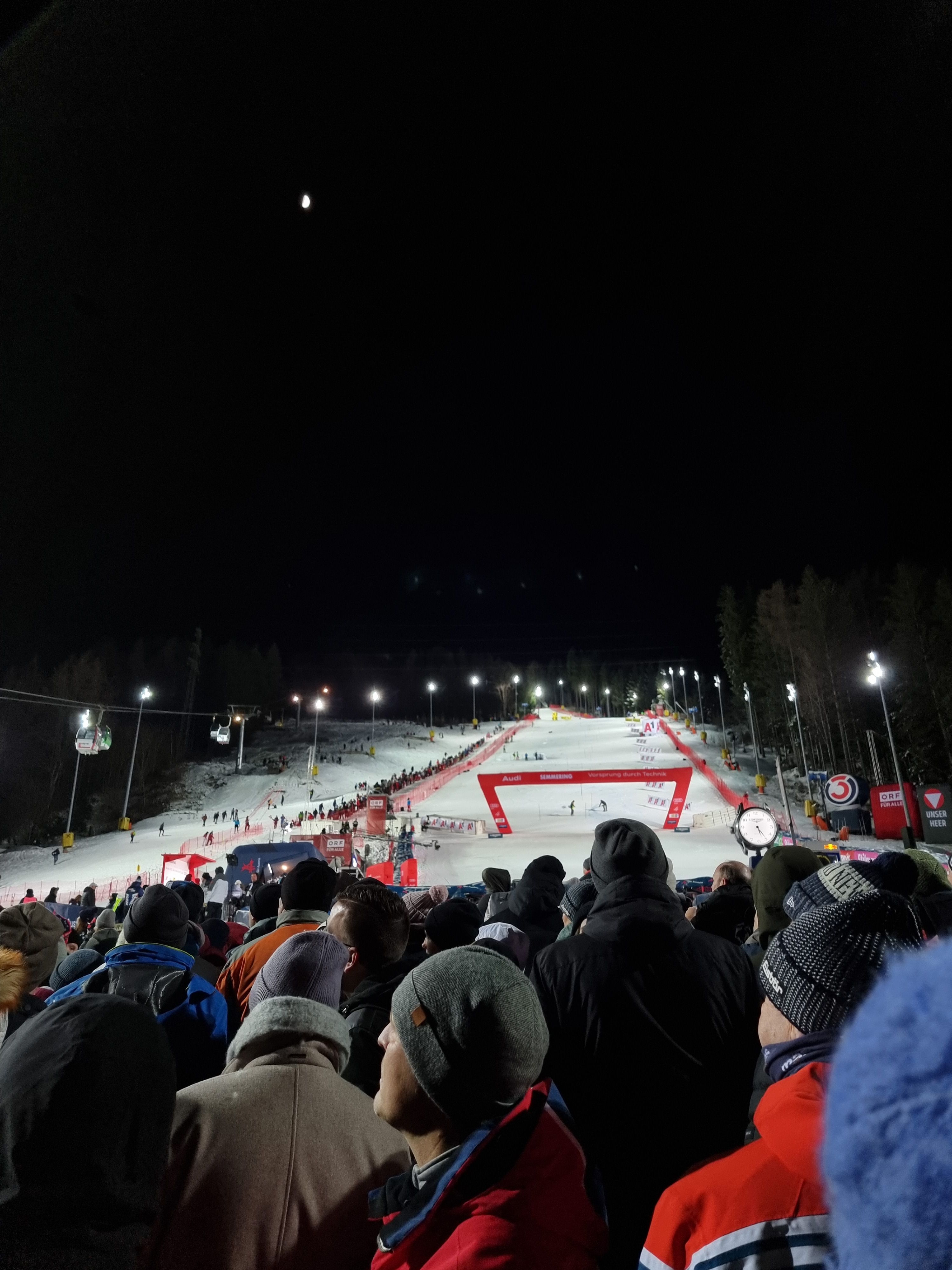 Jubelte Menschen stehen vor dem beleuchteten Zielhang des Skiweltcups bei Nacht