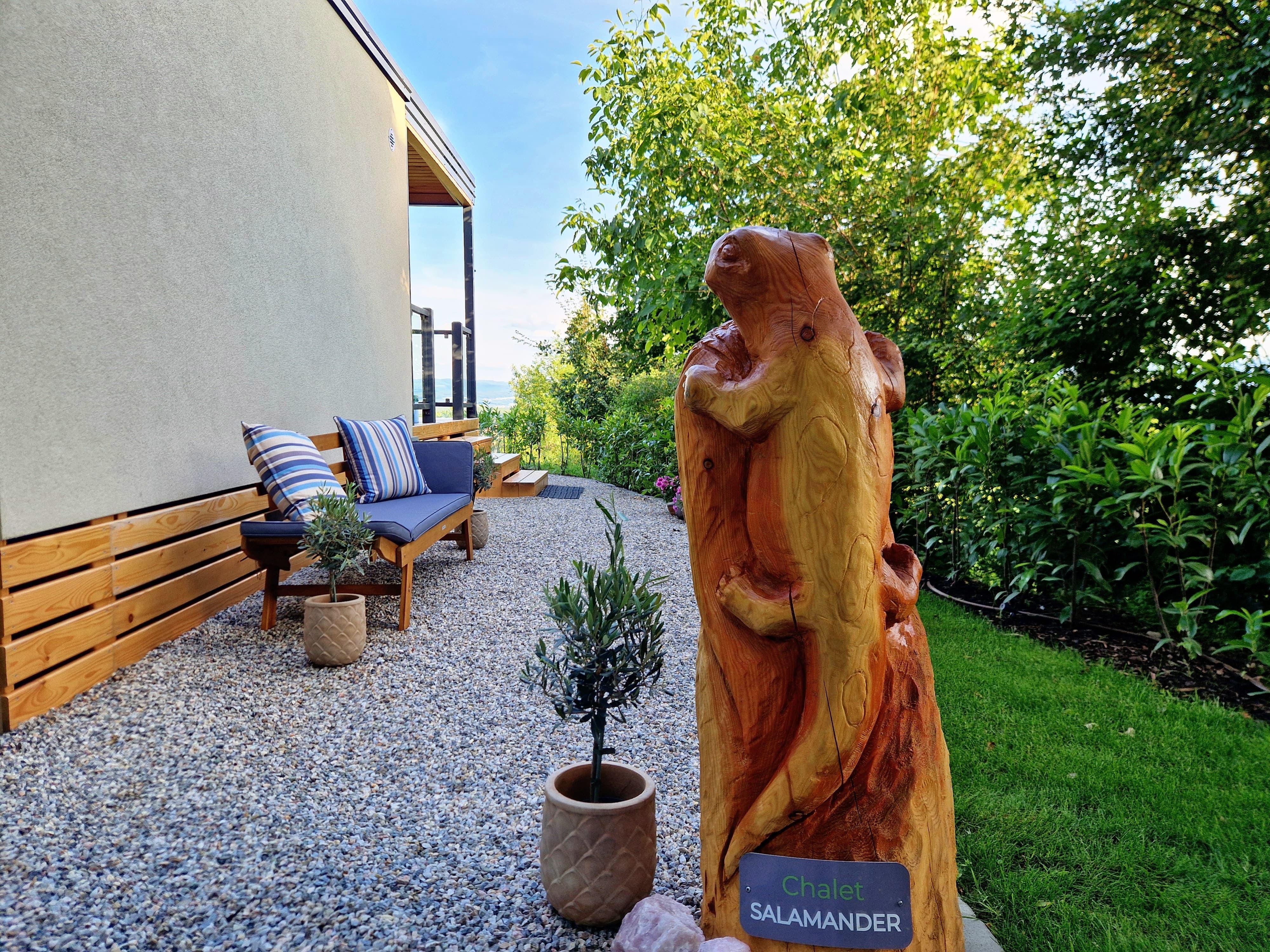 Gartenbereich mit Holzskulptur und Sitzbank beim Chalet Salamander.