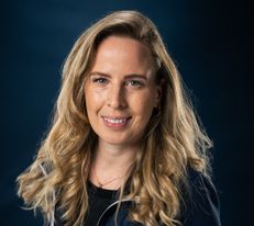 Portraitfoto Wiener Alpen Mitarbeiterin, die eine Jacke mit Wiener Alpen Logo trägt und vor einem dunklem Hintergrund steht.