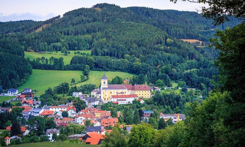 Eine Kirche thront über einem malerischen Dorf, umgeben von grünen Hügeln und Wäldern.