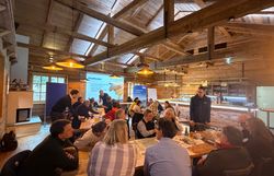 Workshop Teilnehmer diskutieren in Gruppen an drei Tischen in einem rustikalen Raum vor einer Leinwand. 