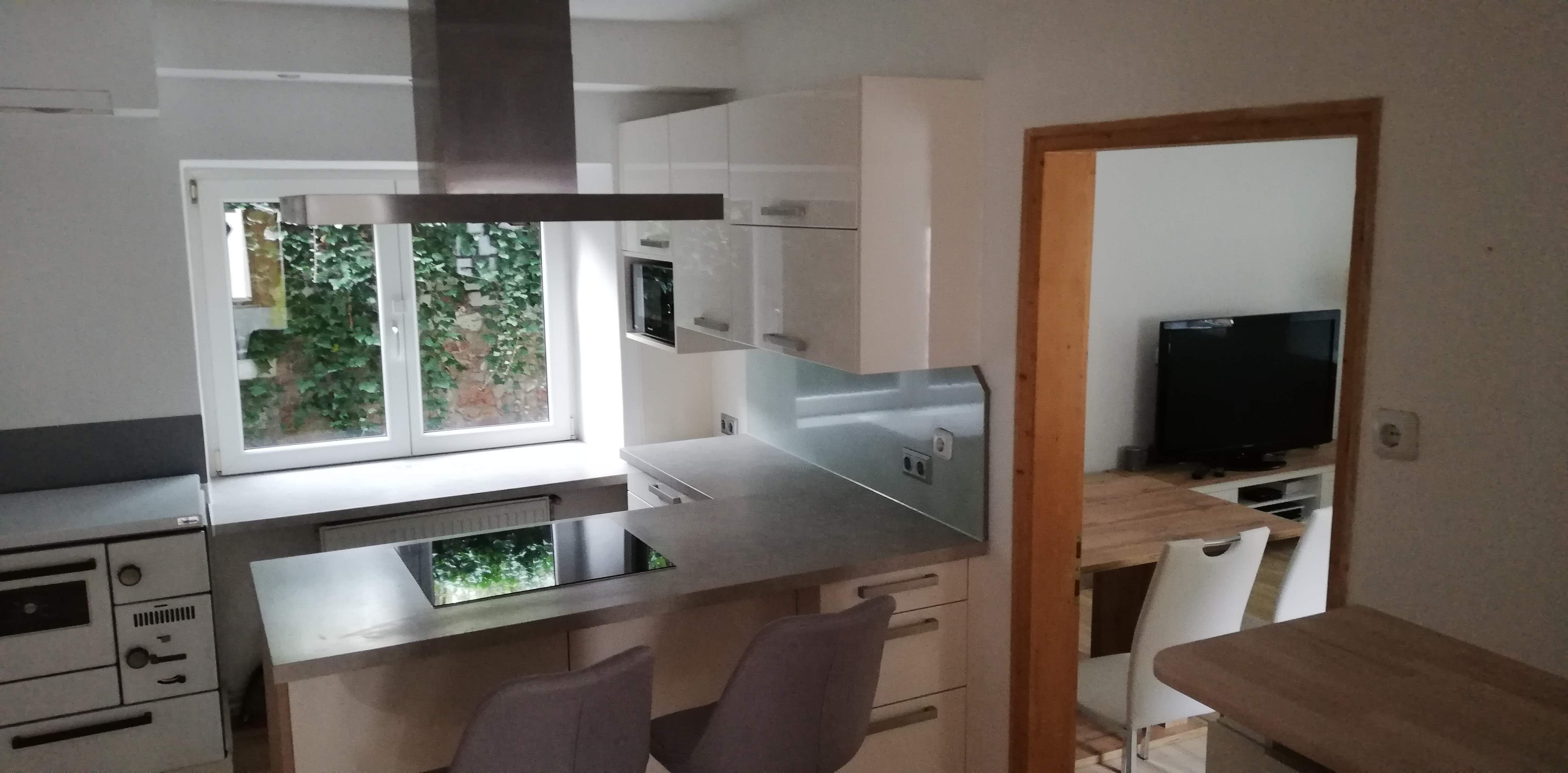 Moderne Küche mit Kochinsel, weißen Schränken und Fenster mit Blick ins Grüne.